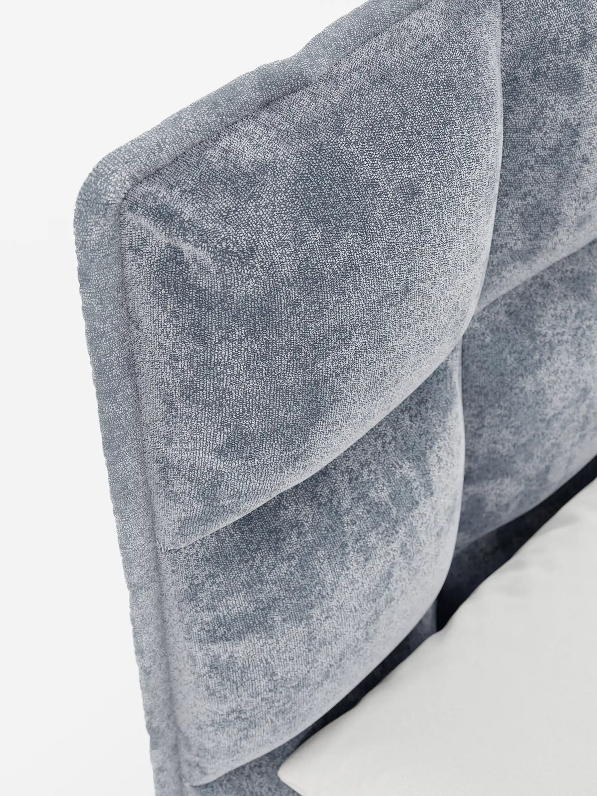 Primo piano del letto imbottito AURO con contenitore e testiera alta capitonné in ciniglia Oeko-Tex® azzurra, caratterizzato da grandi quadrati trapuntati in tessuto testurizzato, con un accenno di biancheria da letto bianca visibile in basso a destra.