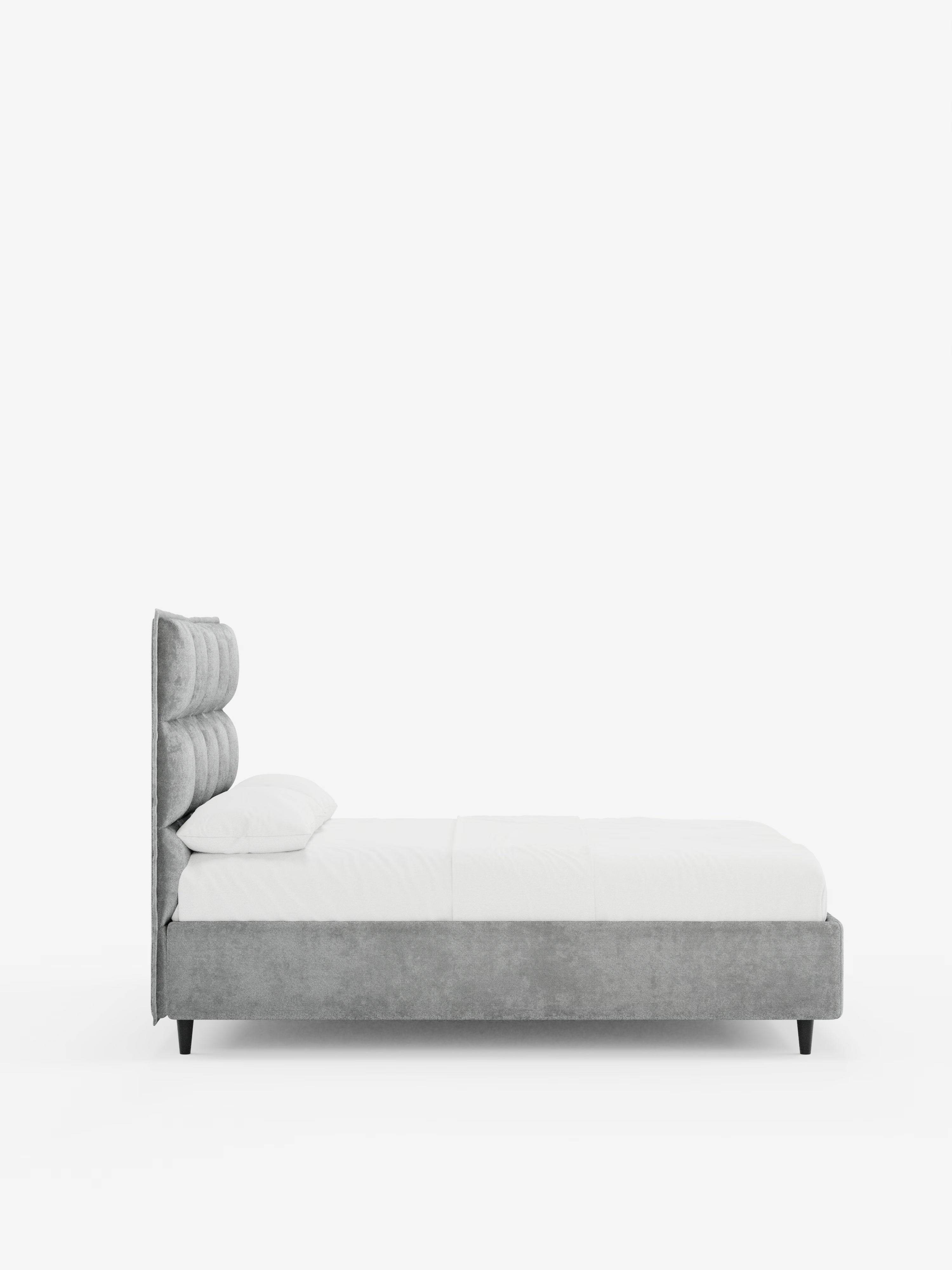 Vista laterale del letto imbottito AURO con contenitore e testiera capitonné alta in ciniglia Oeko-Tex® di Letti.store, caratterizzato da una testiera alta imbottita grigia con capitonné, biancheria da letto bianca e una struttura grigia dal profilo basso con gambe corte nere, il tutto su uno sfondo bianco a tinta unita.
