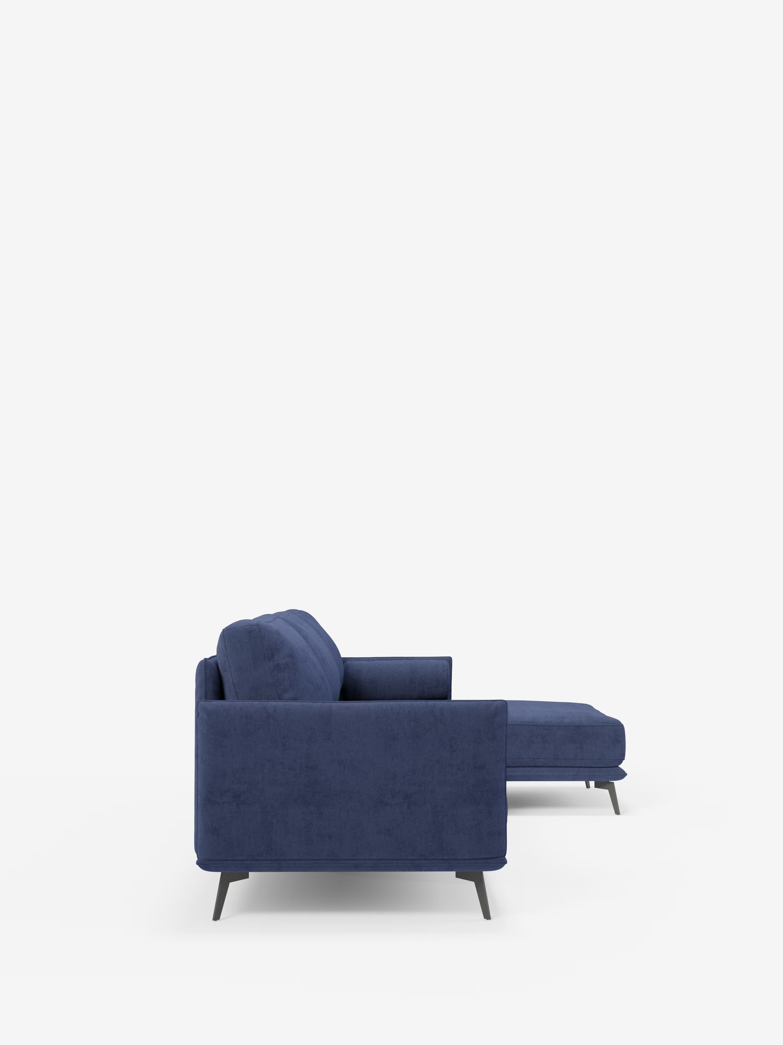 Una vista laterale del divano moderno angolare con penisola “Basalto” di Divani.Modello rivestito in tessuto T31 antimacchia con morbidi cuscini in piuma e base in metallo, caratterizzato da un design contemporaneo blu con chaise longue a destra, braccioli imbottiti, linee pulite e gambe corte scure, su uno sfondo bianco a tinta unita.