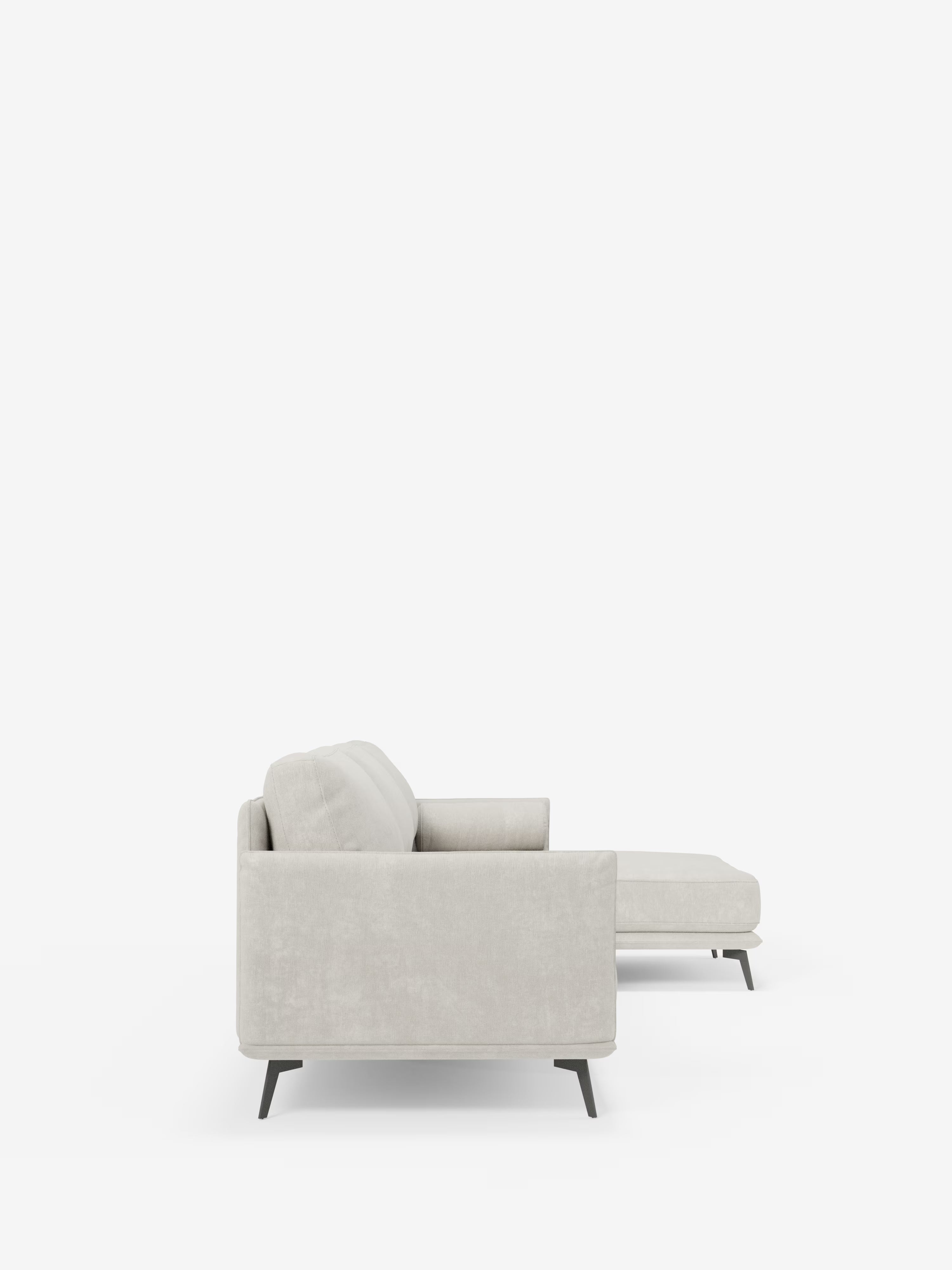 Vista laterale del divano moderno angolare con penisola "Basalto" di Divani.Store, rivestito in tessuto T31 grigio chiaro smacchiabile, con base in metallo nero e cuscini in piuma. Questo divano componibile moderno presenta una chaise longue rivolta verso destra ed è posizionato su uno sfondo bianco a tinta unita, che ne esalta le linee pulite e il design minimalista.