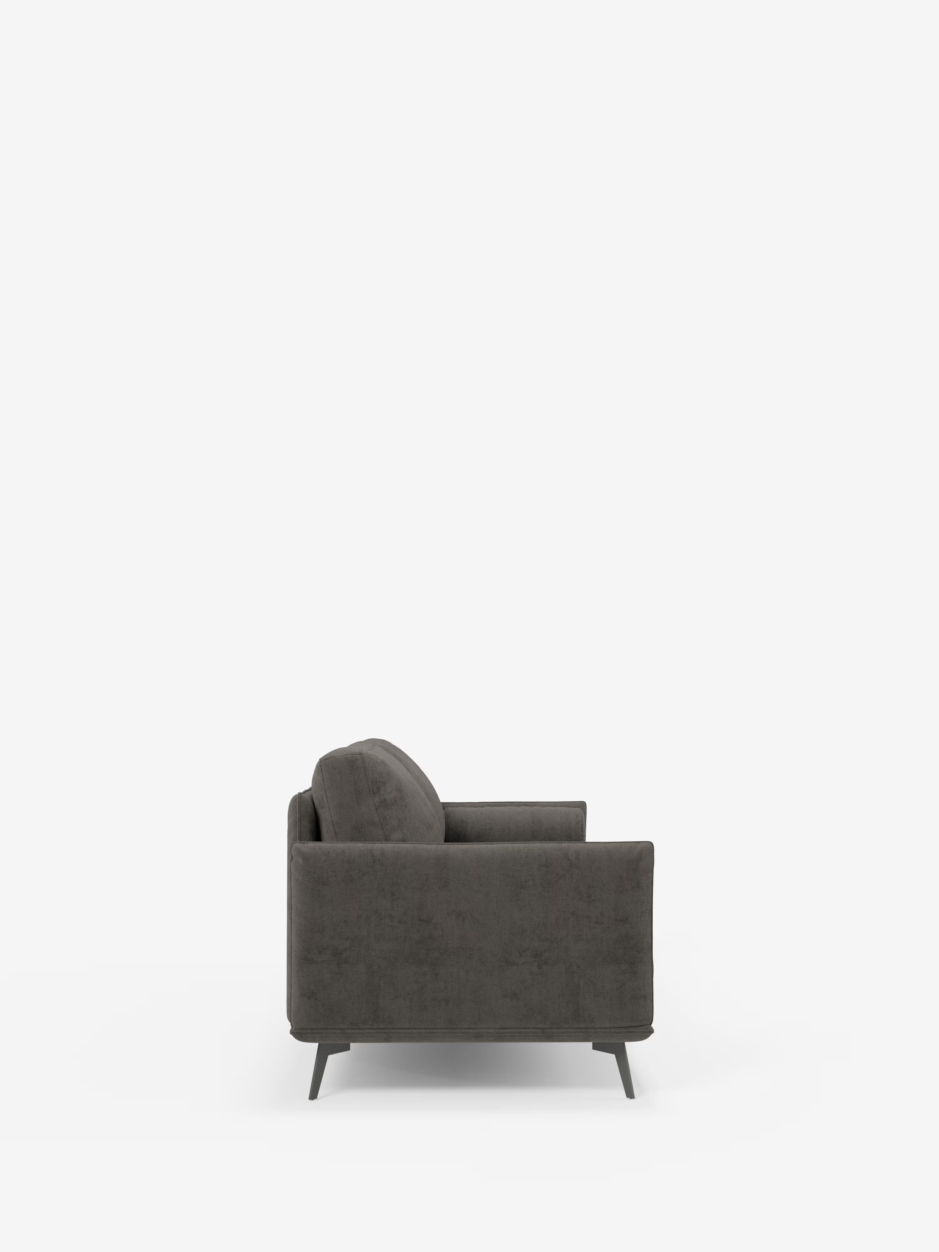 Una vista laterale del divano lineare Basalto a 2 o 3 posti con seduta unica e base in metallo, rivestito in tessuto smacchiabile T31 di Divani.Store, è raffigurata su uno sfondo bianco. Questo divano moderno, di colore grigio scuro, presenta una silhouette squadrata, una morbida seduta a cuscino unico, braccioli bassi e squadrati, gambe scure affusolate e vanta linee pulite dal design minimalista. Il rivestimento sfoderabile aggiunge praticità e versatilità.