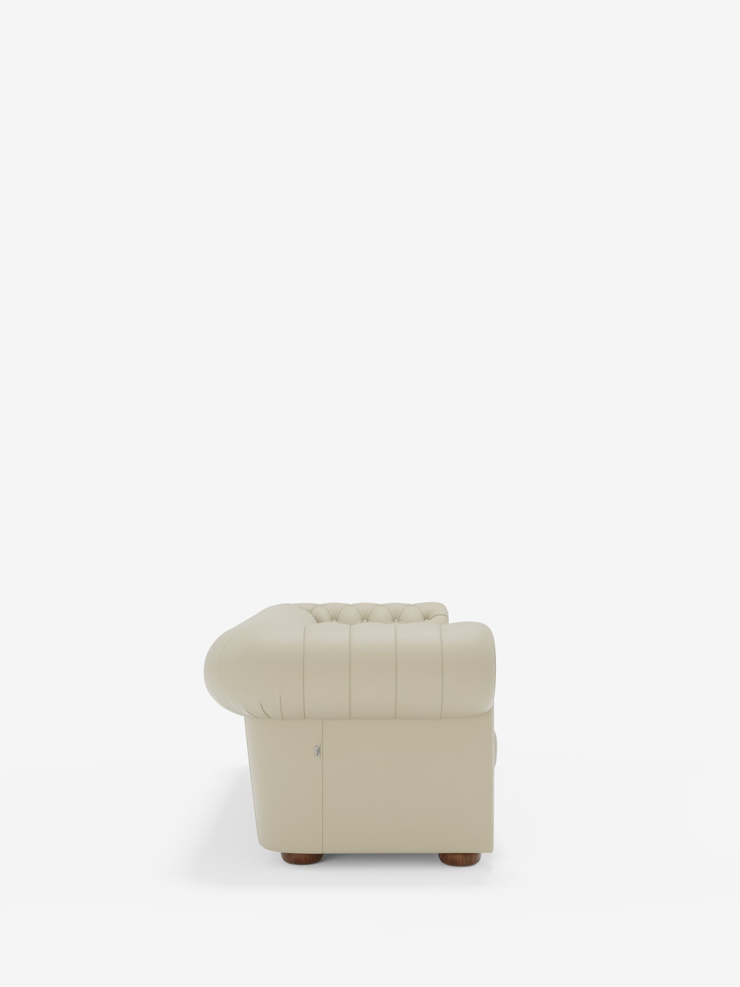 Vista laterale del divano Chester 4 Posti 3 sedute in vera pelle – Chesterfield capitonné artigianale di Divani.Store, caratterizzato da un rivestimento in vera pelle beige con dettagli capitonné e braccioli e schienale arrotondati, poggiato su piccoli piedini rotondi in legno. Lo sfondo bianco a tinta unita mette in risalto la forma artigianale e la raffinata lavorazione di questo divano Chesterfield.