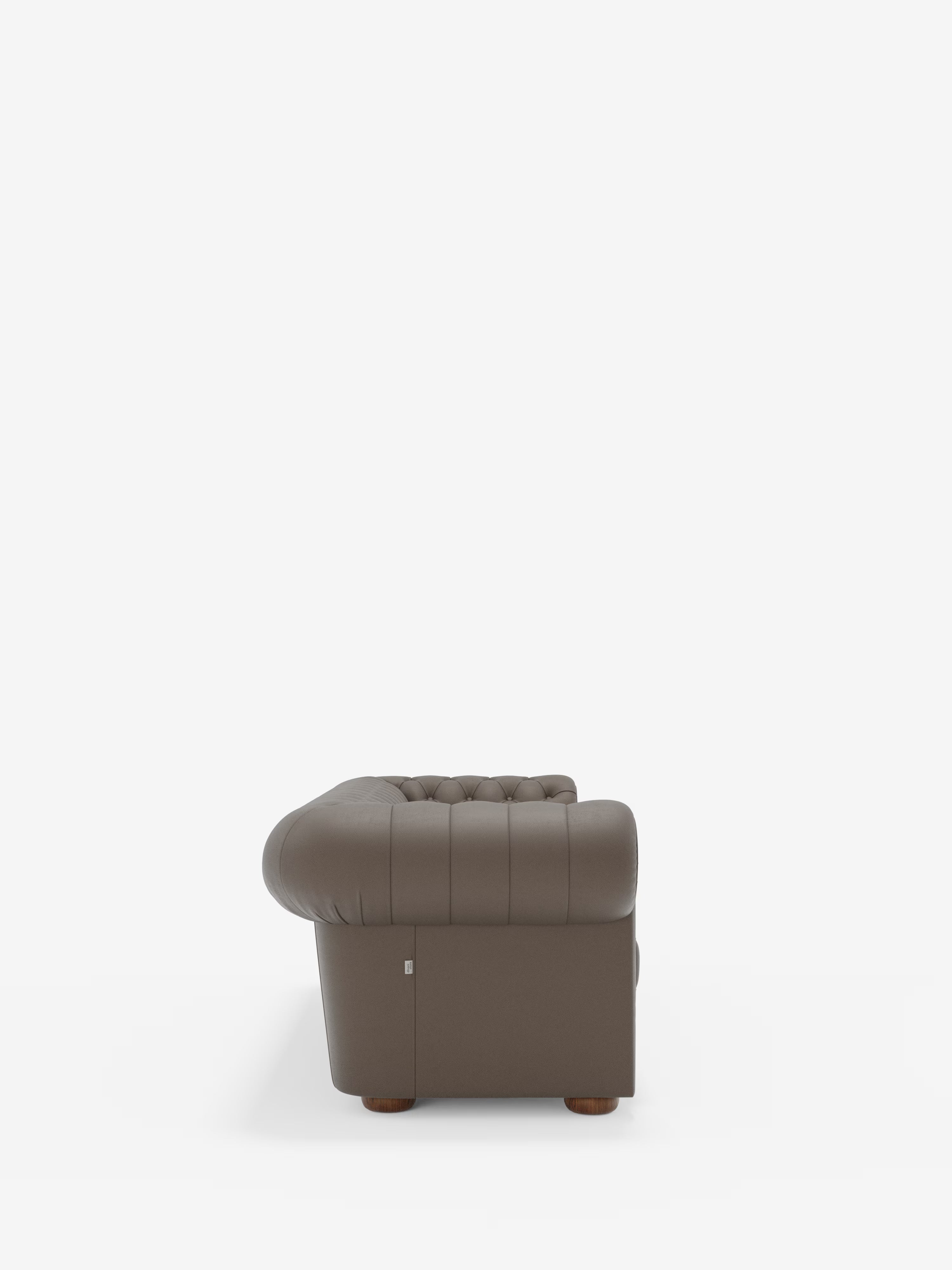 Vista laterale della poltrona Chester 4 Posti 3 sedute in Vera Pelle – Chesterfield Capitonné Artigianale di Divani.Store, una poltrona marrone trapuntata con braccioli arrotondati e rivestimento in vera pelle cucita. La poltrona presenta gambe corte in legno, mentre lo sfondo bianco a tinta unita ne esalta la forma distintiva e il design artigianale.