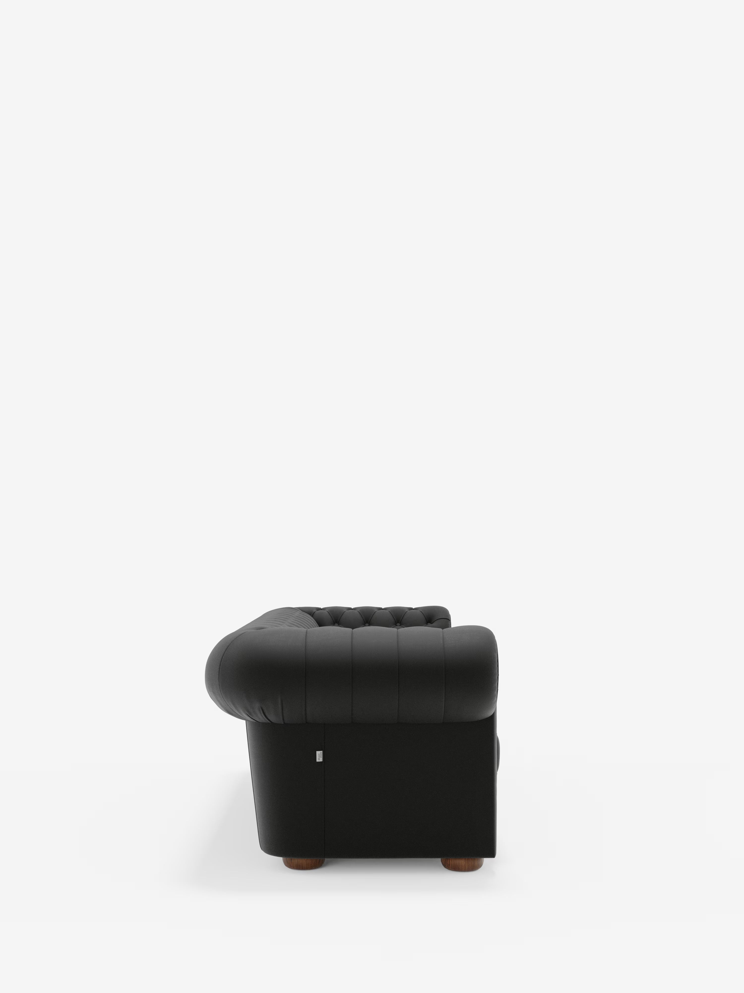 Vista laterale della Chester 4 Posti 3 sedute in Vera Pelle – Chesterfield Capitonné Artigianale di Divani.Store, una poltrona nera trapuntata con braccioli arrotondati e piedini in legno, su uno sfondo bianco a tinta unita. Ispirata al classico design Chesterfield, questa poltrona è rivestita in morbida vera pelle, con un'imbottitura compatta e una finitura leggermente lucida che ne esalta la raffinata lavorazione artigianale.