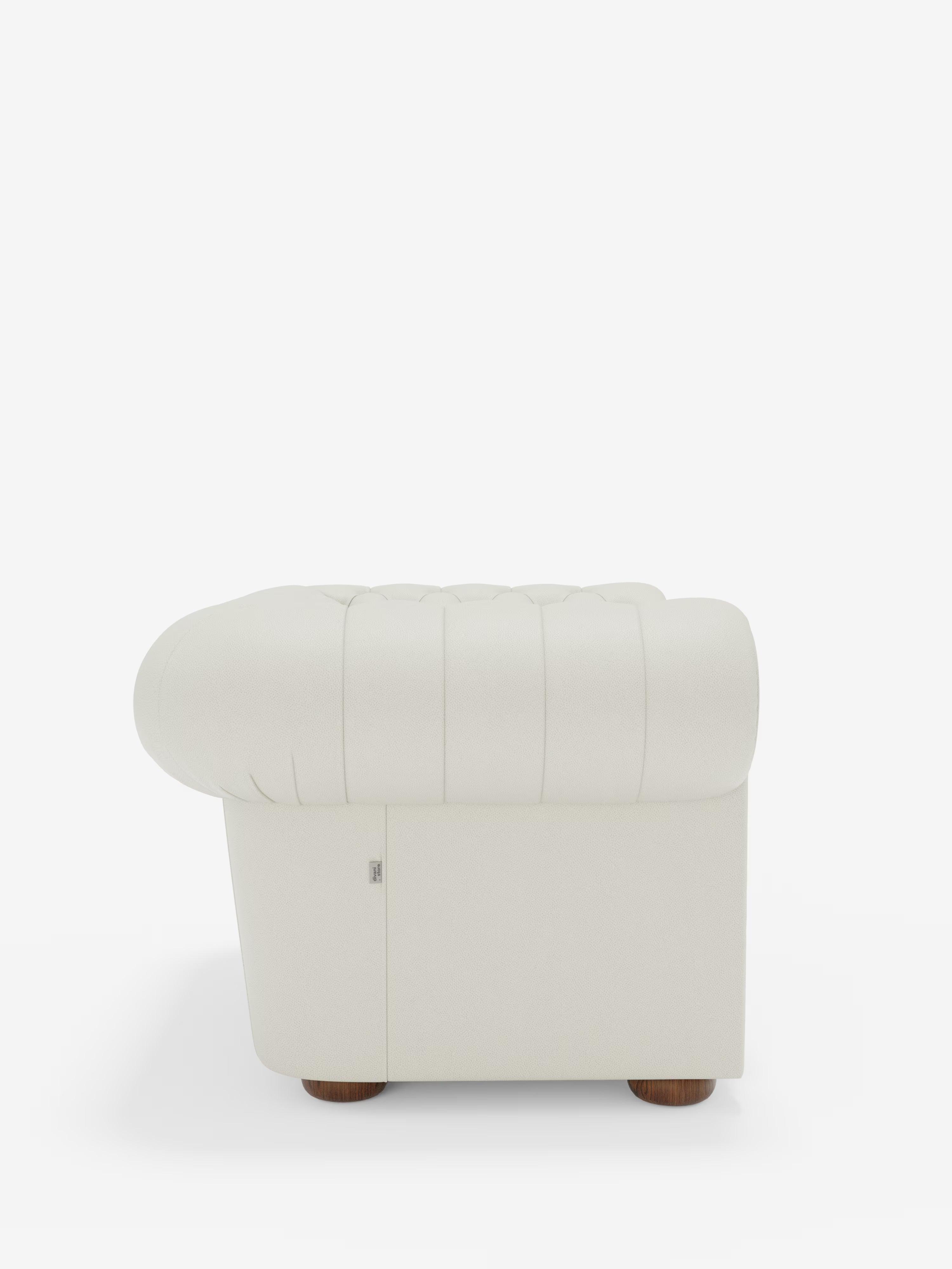 Vista laterale della poltrona Chester in vera pelle spessorata con capitonné artigianale di Divani.Store, caratterizzata da un design color crema con trapuntatura ispirata al classico stile delle poltrone capitonné. La poltrona presenta braccioli arrotondati, gambe corte in legno e un aspetto morbido e imbottito. Su uno sfondo bianco a tinta unita, la poltrona spicca come elemento centrale dell’immagine.