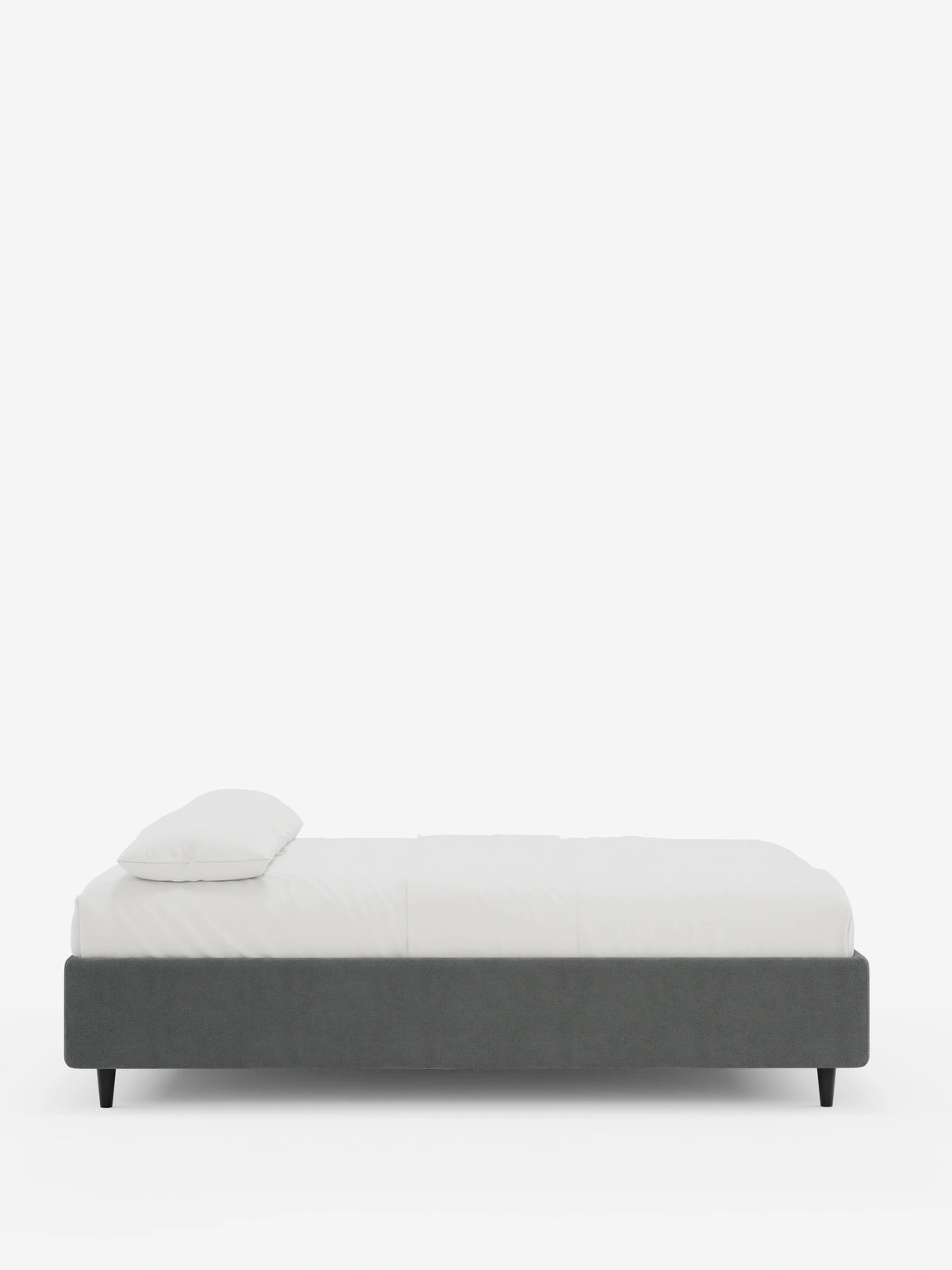 Vista laterale di un letto sommier imbottito ERON con vano contenitore in tessuto impermeabile certificato Oeko-Tex, con struttura imbottita grigio scuro, materasso bianco, un cuscino e quattro gambe corte e affusolate di colore nero su sfondo bianco.