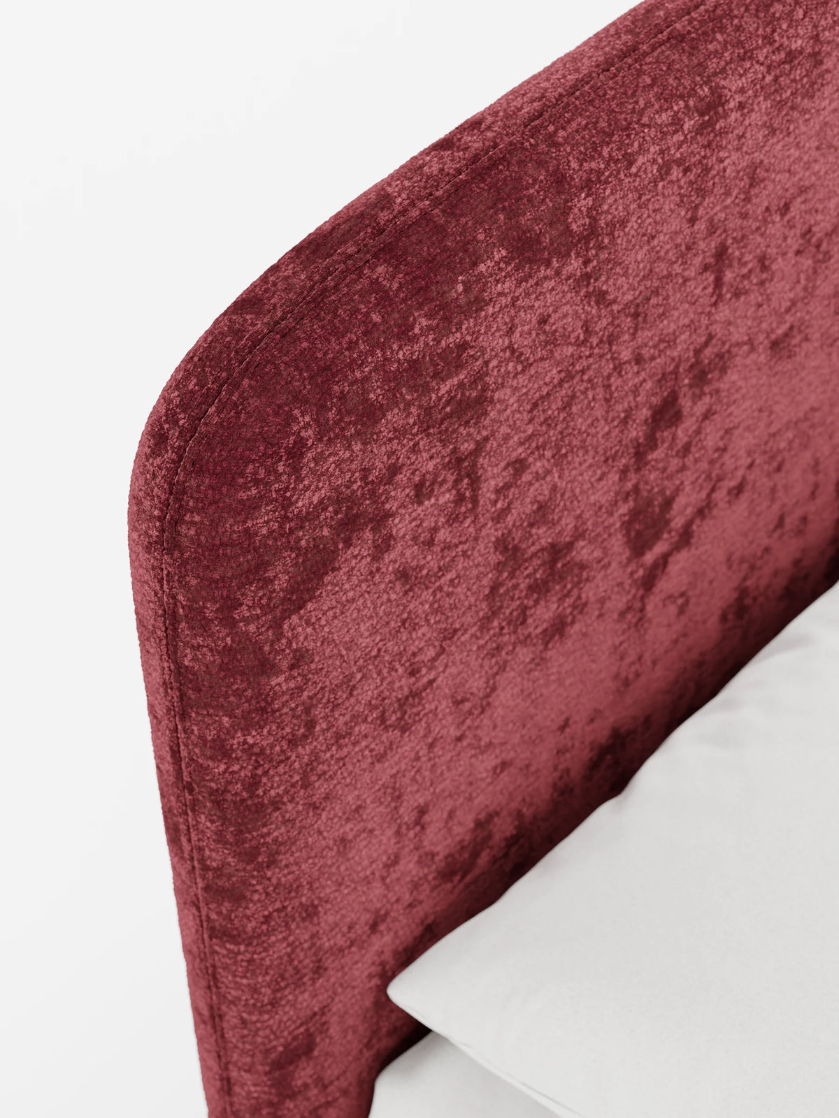Un primo piano del letto imbottito KAELOS Letto Minimal, caratterizzato da una testiera arrotondata in ciniglia ruvida di colore rosso intenso su sfondo bianco, con un cuscino grigio chiaro posizionato sotto.