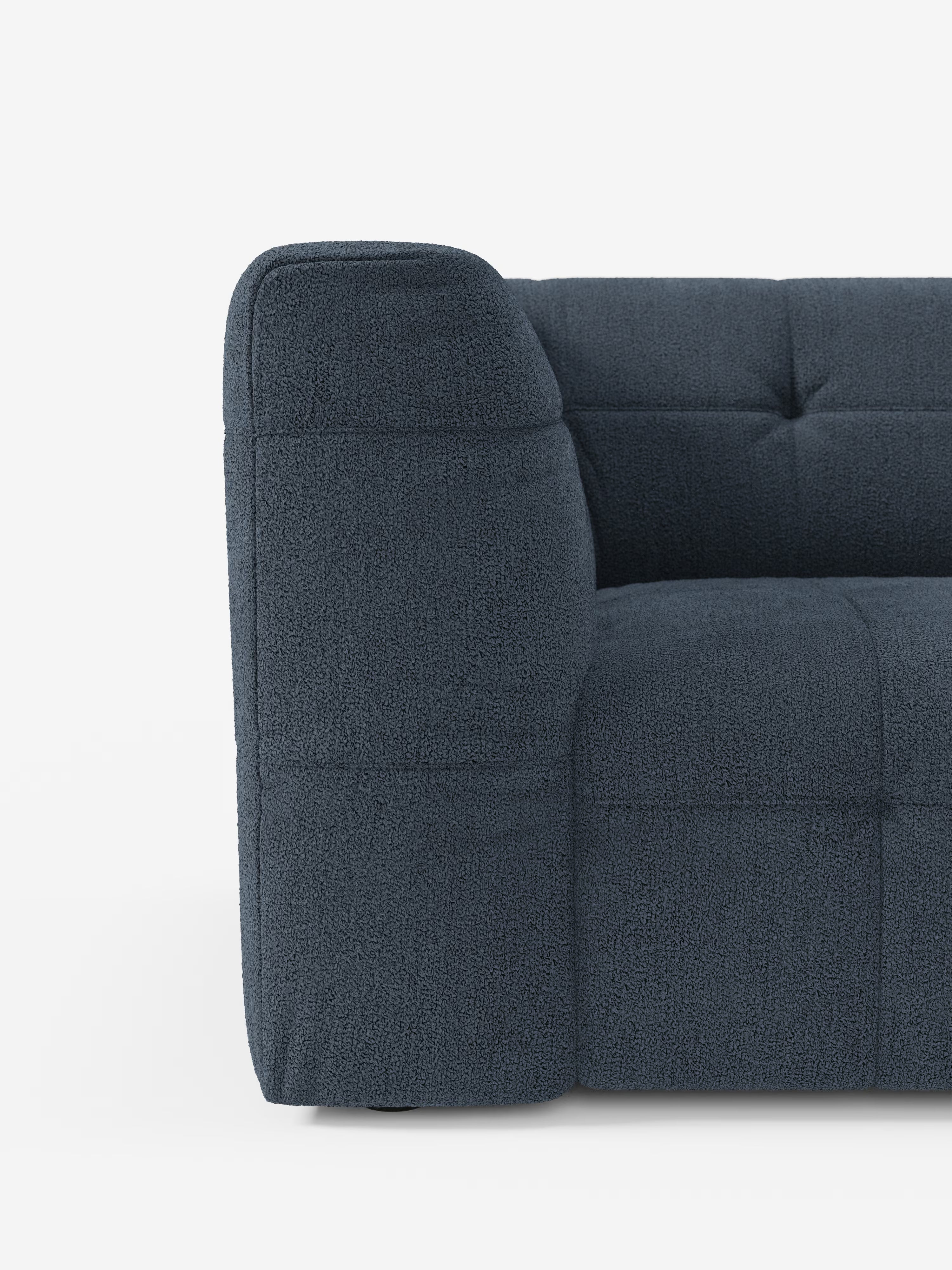 Primo piano della vista laterale del divano angolare componibile e modulare Mosaic in bouclé di Divani.Store, realizzato in tessuto T21 blu navy intenso, resistente alle macchie, con motivo capitonné. Questo divano moderno si contraddistingue per le linee pulite, i braccioli bassi e le cuciture a capitonné a vista sia sulla seduta che sullo schienale: un'aggiunta elegante a qualsiasi soggiorno moderno, fotografato su uno sfondo bianco a tinta unita.