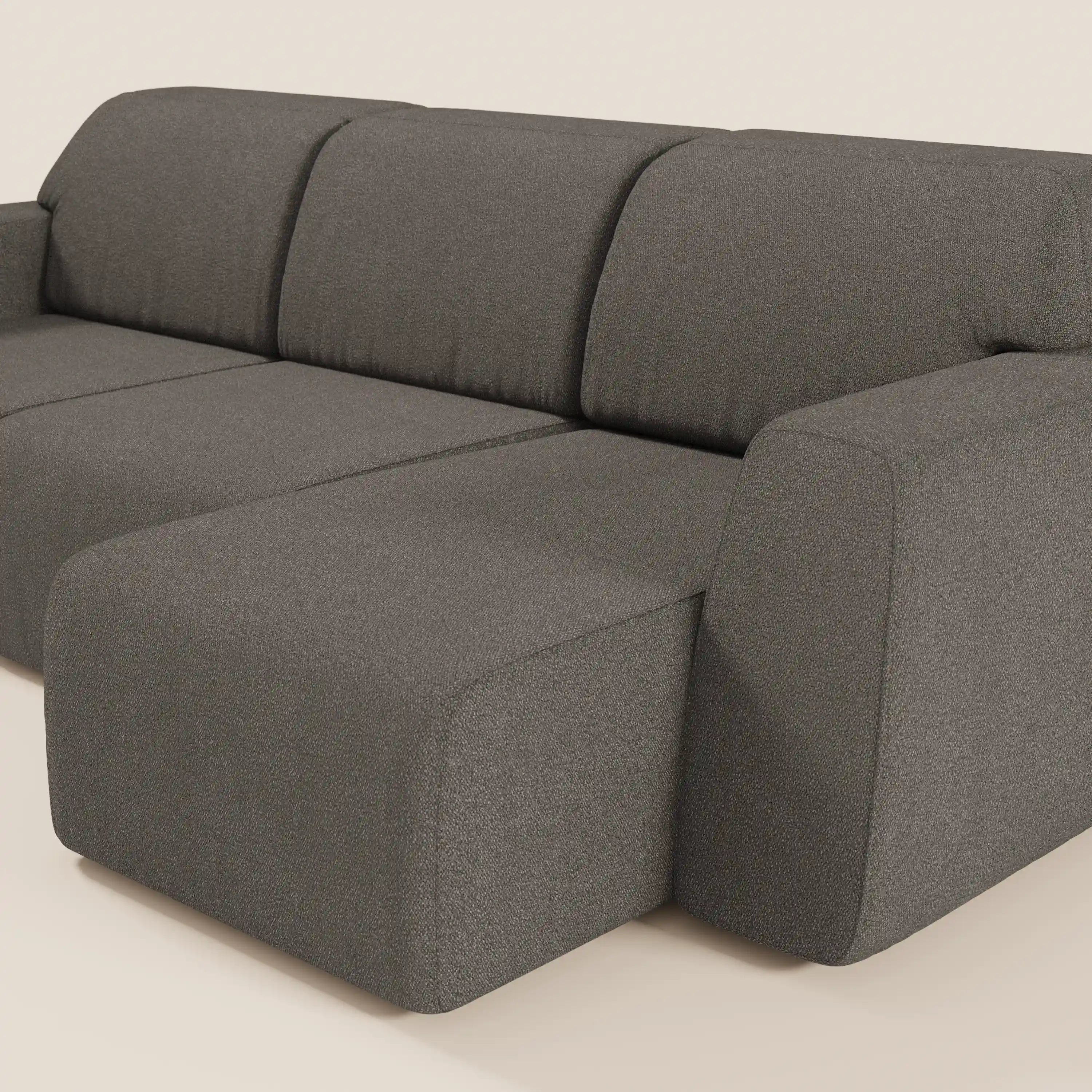 Il divano Orbit con 3 sedute scorrevoli e allungabili di Divani.Store, in tessuto grigio scuro effetto cotone T33, è caratterizzato da ampi braccioli arrotondati e da una chaise lounge a sinistra, presentata su uno sfondo beige chiaro dallo stile minimalista.