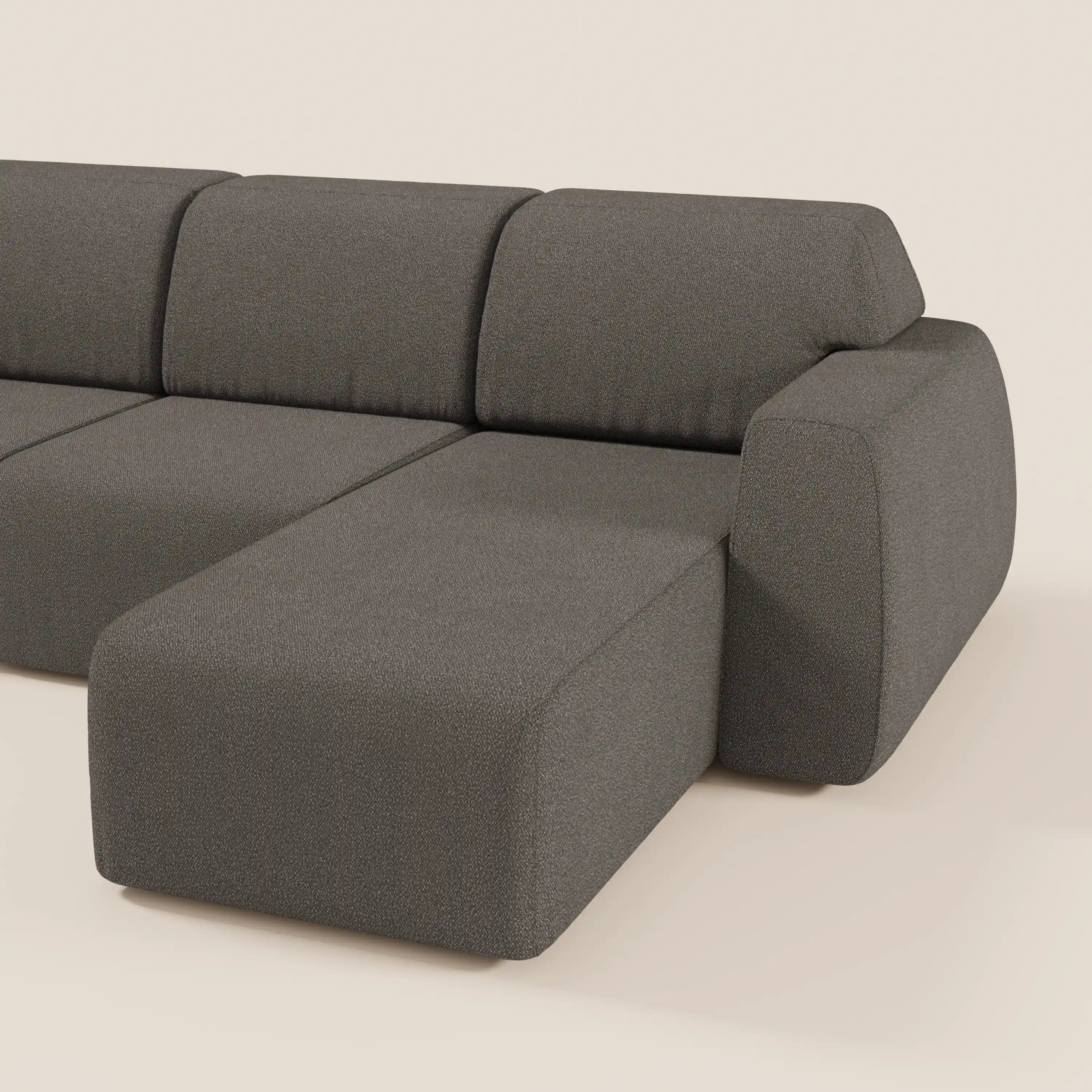 Il divano angolare Orbit di Divani.Store è caratterizzato da una chaise reversibile e da sedute allungabili in tessuto T33 antimacchia effetto cotone, con cuscini a blocchi e un design minimalista a basso profilo in grigio scuro su sfondo beige chiaro.