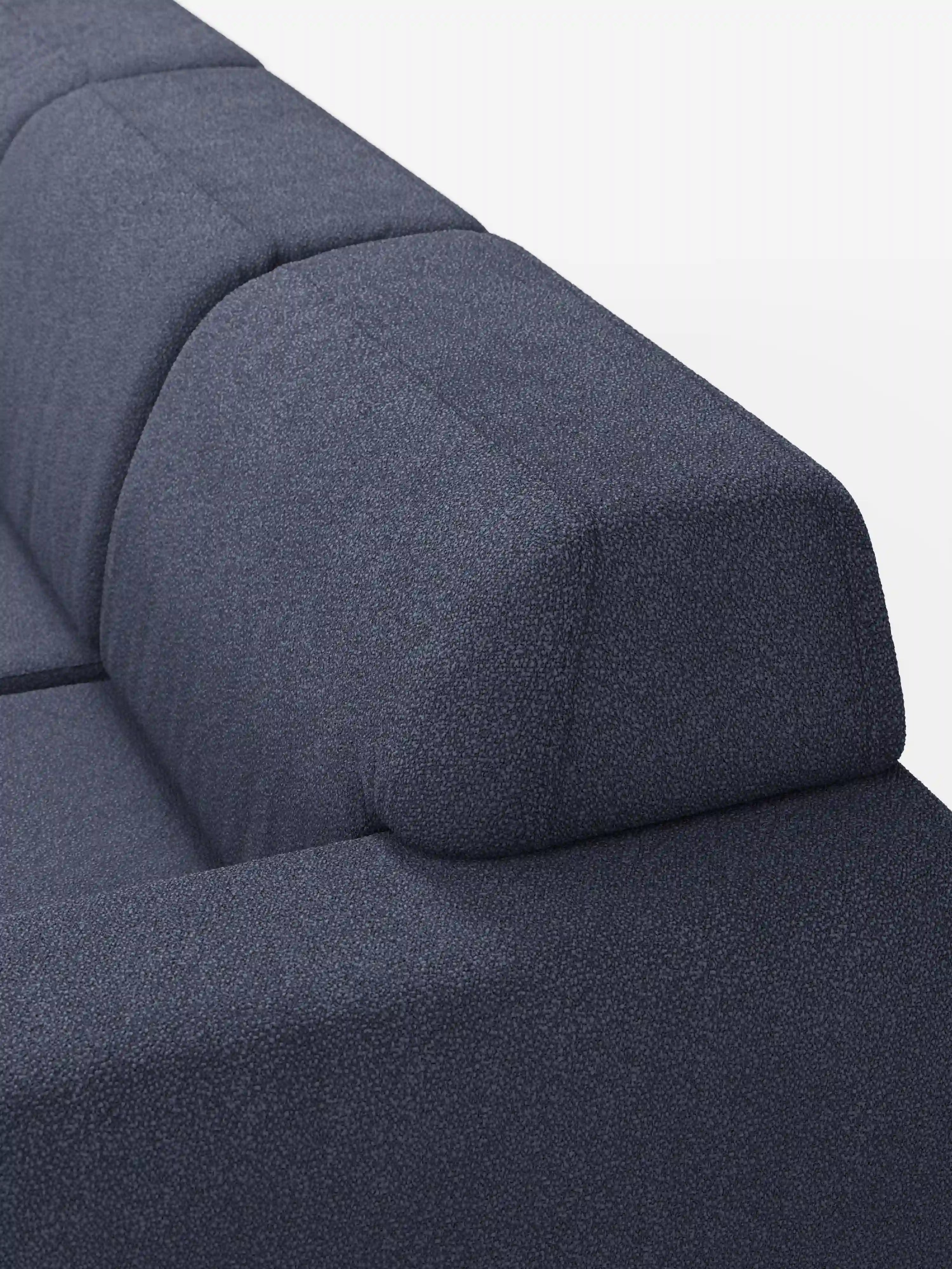Un primo piano dell’Orbit Divano angolare con penisola reversibile e tutte le sedute allungabili in tessuto smacchiabile effetto cotone T33 di Divani.Store mette in risalto il suo tessuto testurizzato, di colore blu scuro, resistente alle macchie ed effetto cotone, le linee pulite e lo schienale angolato. L'immagine mette in risalto il bracciolo e lo schienale su uno sfondo bianco a tinta unita.