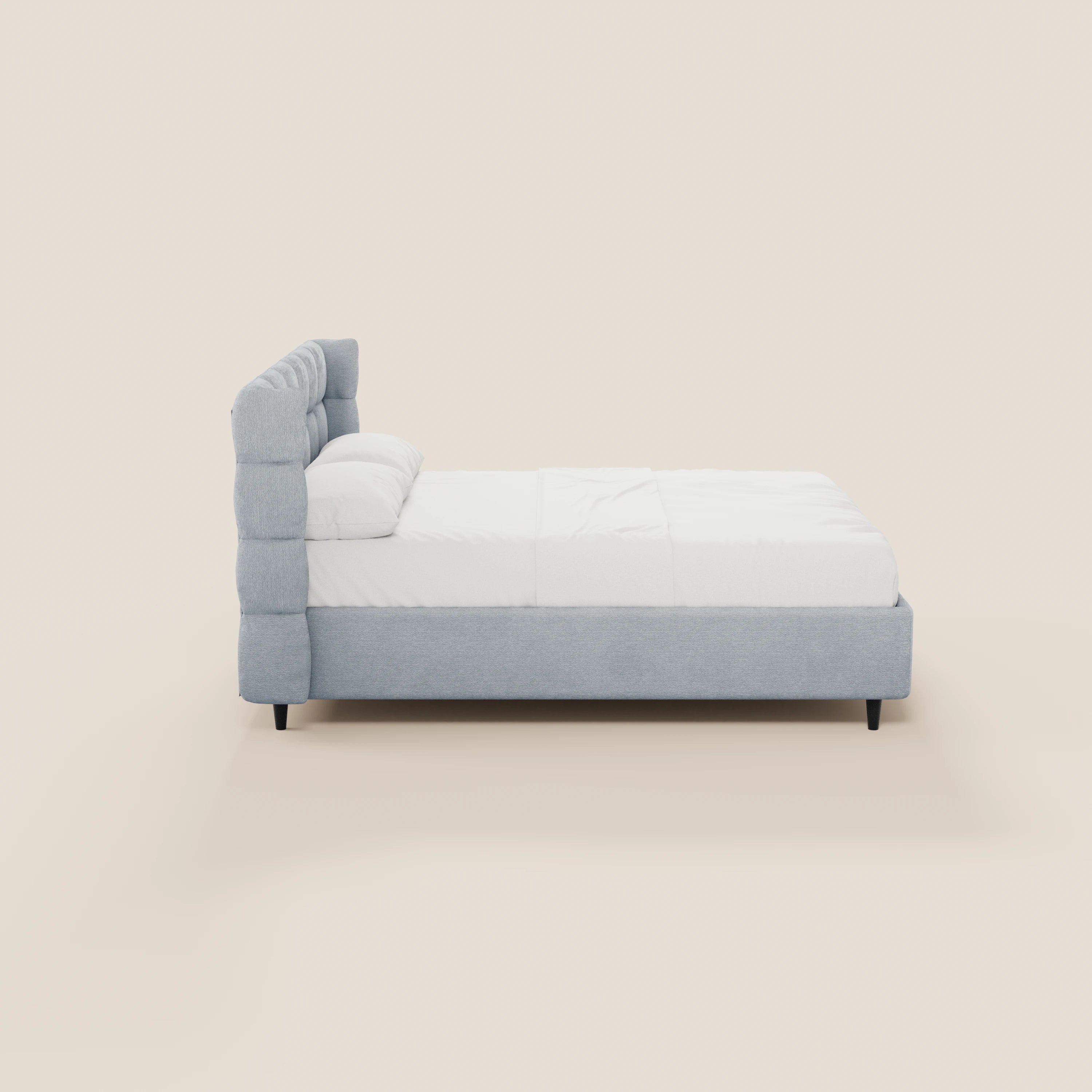Il letto imbottito RAGNAR di Letti.store è caratterizzato da un tessuto grigio chiaro certificato Oeko-Tex®, una testiera capitonné avvolgente, biancheria da letto bianca, due cuscini, gambe corte nere e un design moderno e minimalista, ripreso di profilo su uno sfondo bianco sporco.