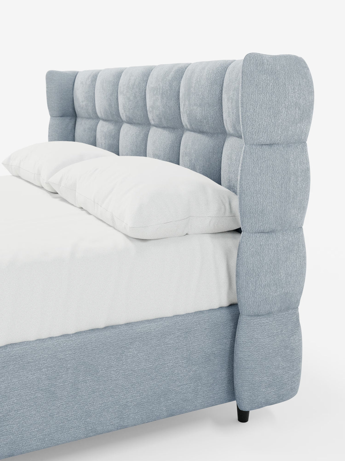 Un moderno letto imbottito RAGNAR con contenitore di Letti.store, caratterizzato da un elegante tessuto certificato Oeko-Tex® in azzurro. L’avvolgente testiera capitonné del letto presenta ampie sezioni quadrate e morbide che conferiscono al letto un aspetto lussuoso e imbottito. Allestito con cura con biancheria da letto e cuscini bianchi, le morbide trame del letto risaltano sullo sfondo bianco uniforme.