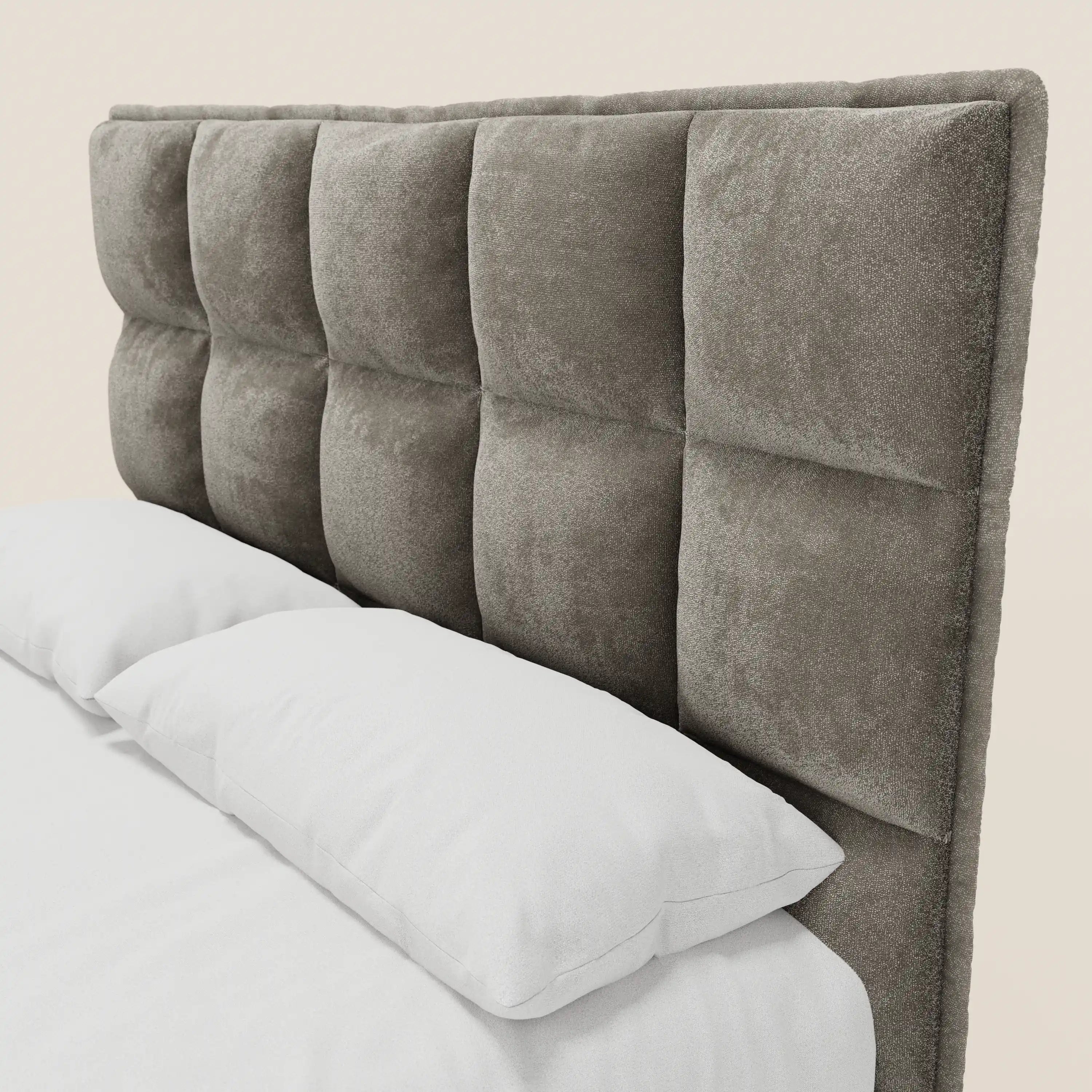 Un primo piano del letto imbottito AURO di Letti.store, caratterizzato da una testiera alta e morbida in ciniglia certificata Oeko-Tex® con un motivo capitonné a quadrati. I cuscini e le lenzuola bianchi creano un contrasto suggestivo con la sua superficie morbida e dai toni neutri.