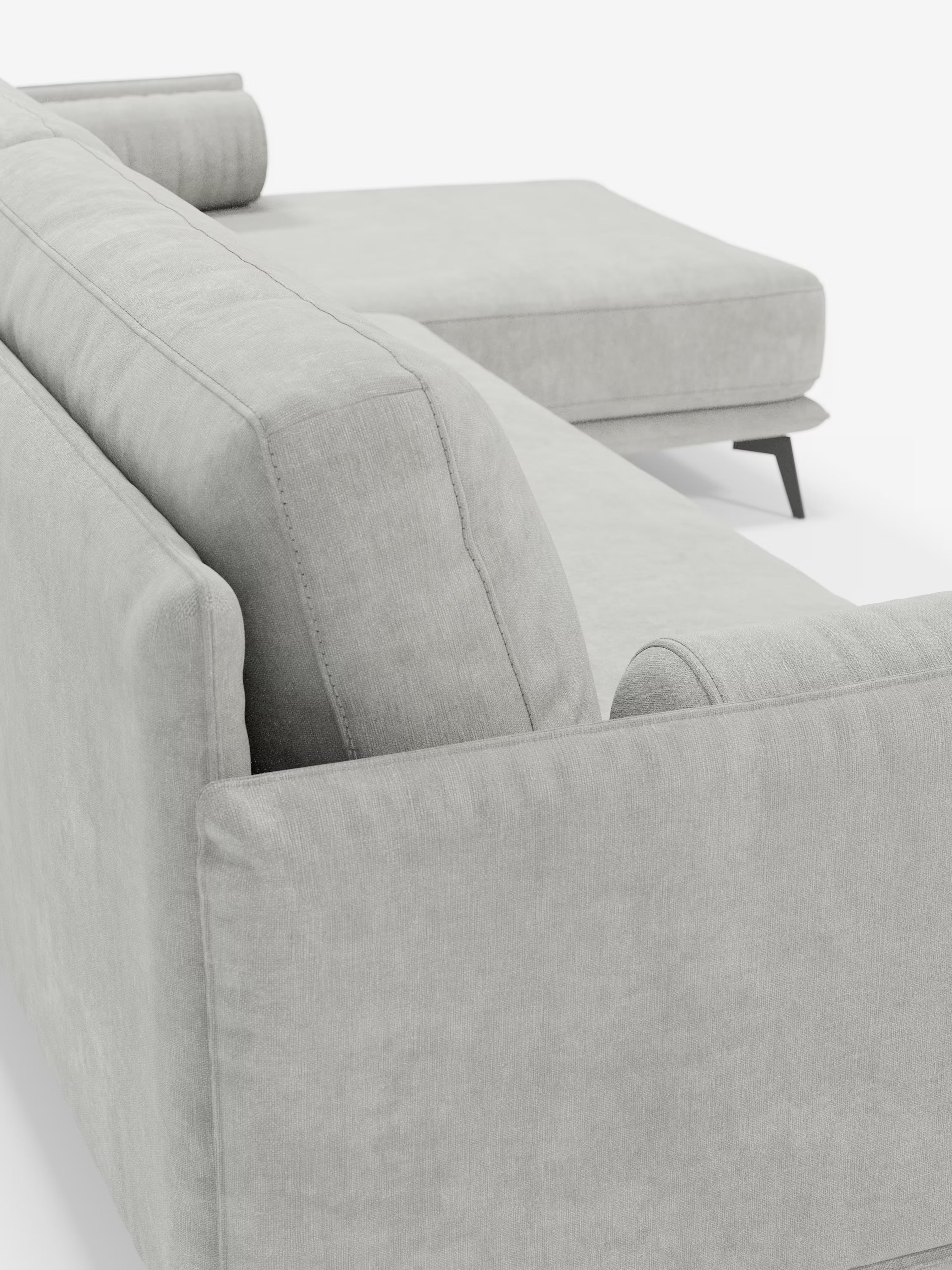 Primo piano del divano moderno angolare con penisola “Basalto” di Divani.Store, qui presentato in tessuto T31 grigio chiaro e resistente alle macchie. Questo divano di produzione italiana è dotato di una chaise longue, di un’elegante base in metallo nero, di morbidi cuscini in piuma e di un cuscino cilindrico per un comfort ancora maggiore. Le linee pulite risaltano sullo sfondo bianco a tinta unita.