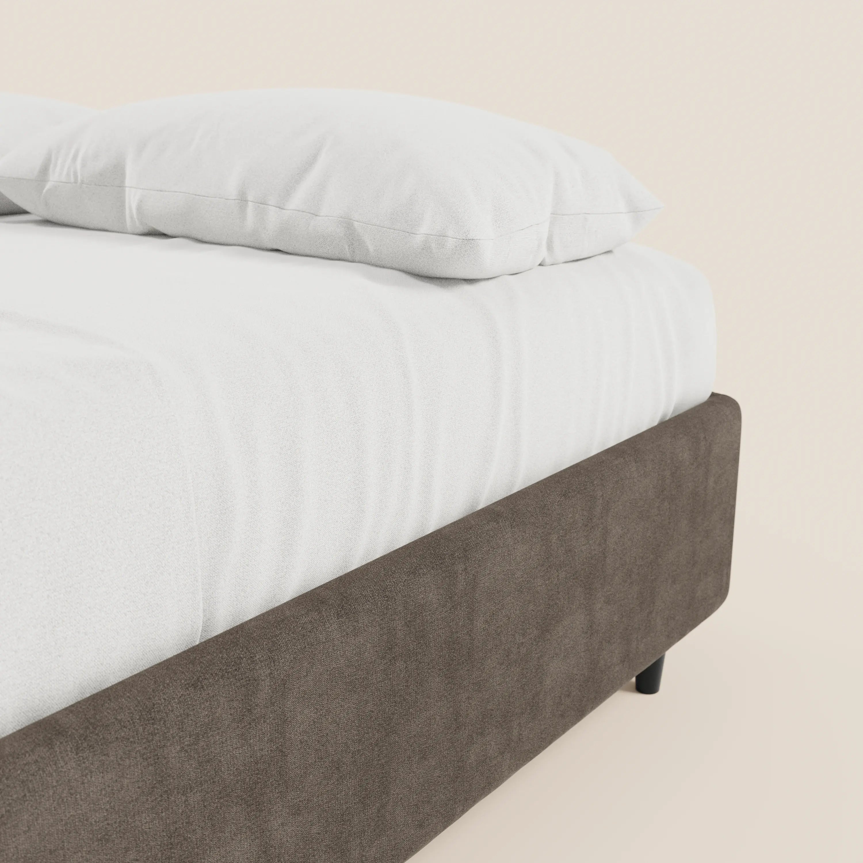 Un primo piano del letto sommier imbottito ERON di Letti.store mostra un lenzuolo bianco e un cuscino su una struttura del letto in tessuto impermeabile marrone certificato Oeko-Tex, con gambe corte nere e un vano contenitore, il tutto su uno sfondo chiaro.