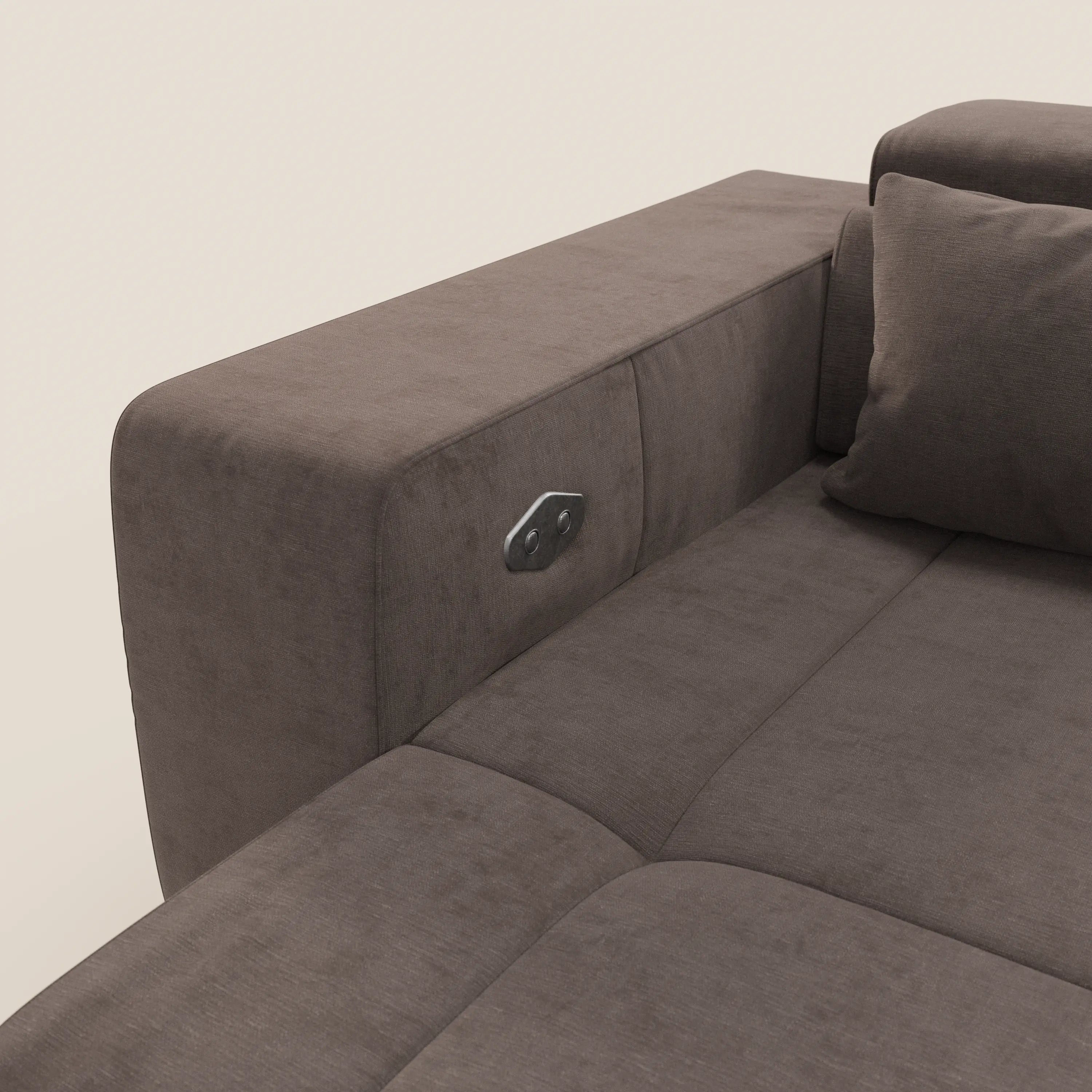 Primo piano di Monarch Divano angolare con penisola e Relax Elettrico di Divani.Store, in tessuto antimacchia T31 marrone. Bracciolo sinistro con presa di corrente argentata incorporata, cuscini di seduta e di schienale in tessuto morbido, sfondo beige.