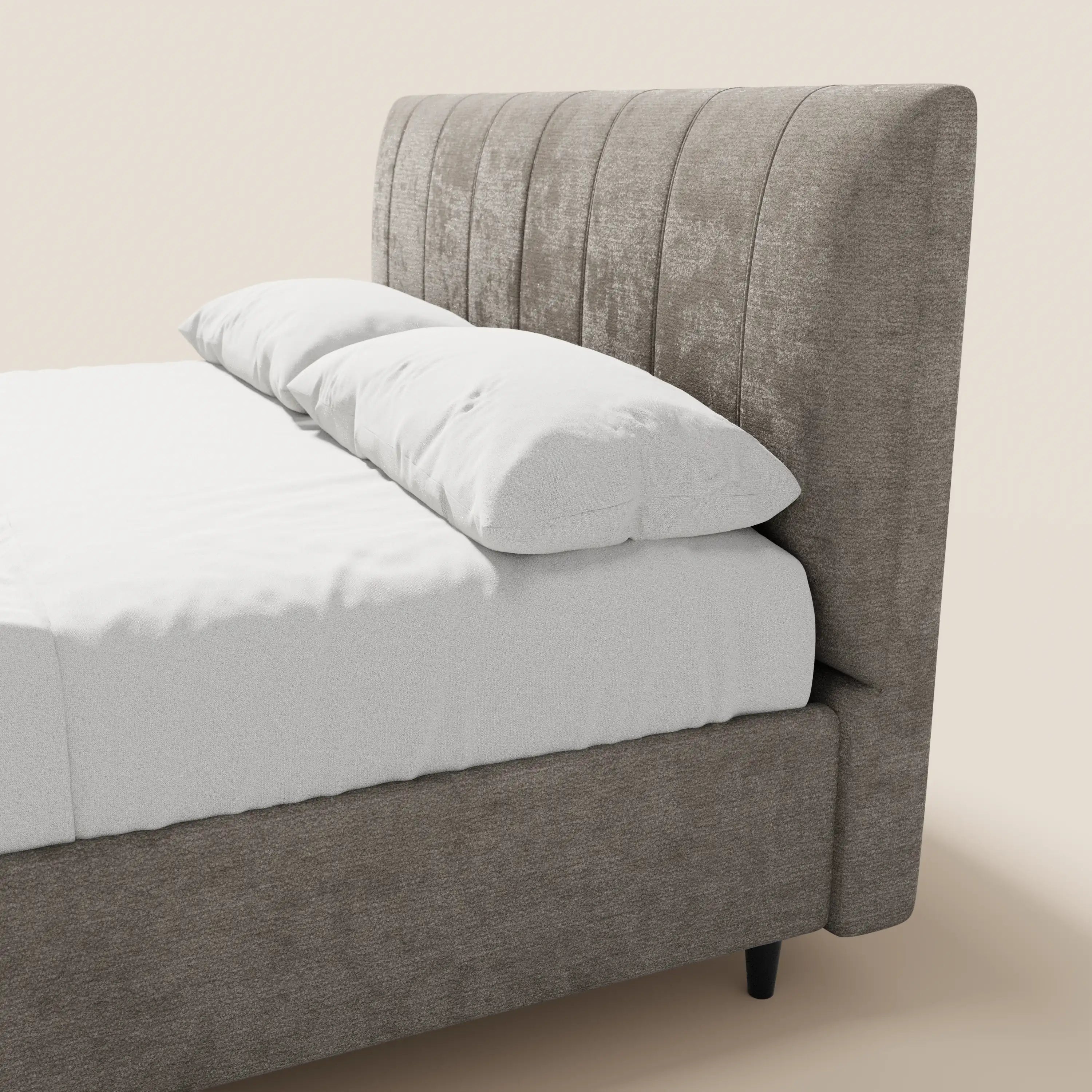 Una vista laterale ravvicinata del letto imbottito con contenitore ONYX di Letti.store, caratterizzato da una testiera alta e verticale in tessuto color taupe certificato Oeko-Tex®, biancheria da letto bianca, cuscini impilati e gambe corte nere su uno sfondo a tinta unita.