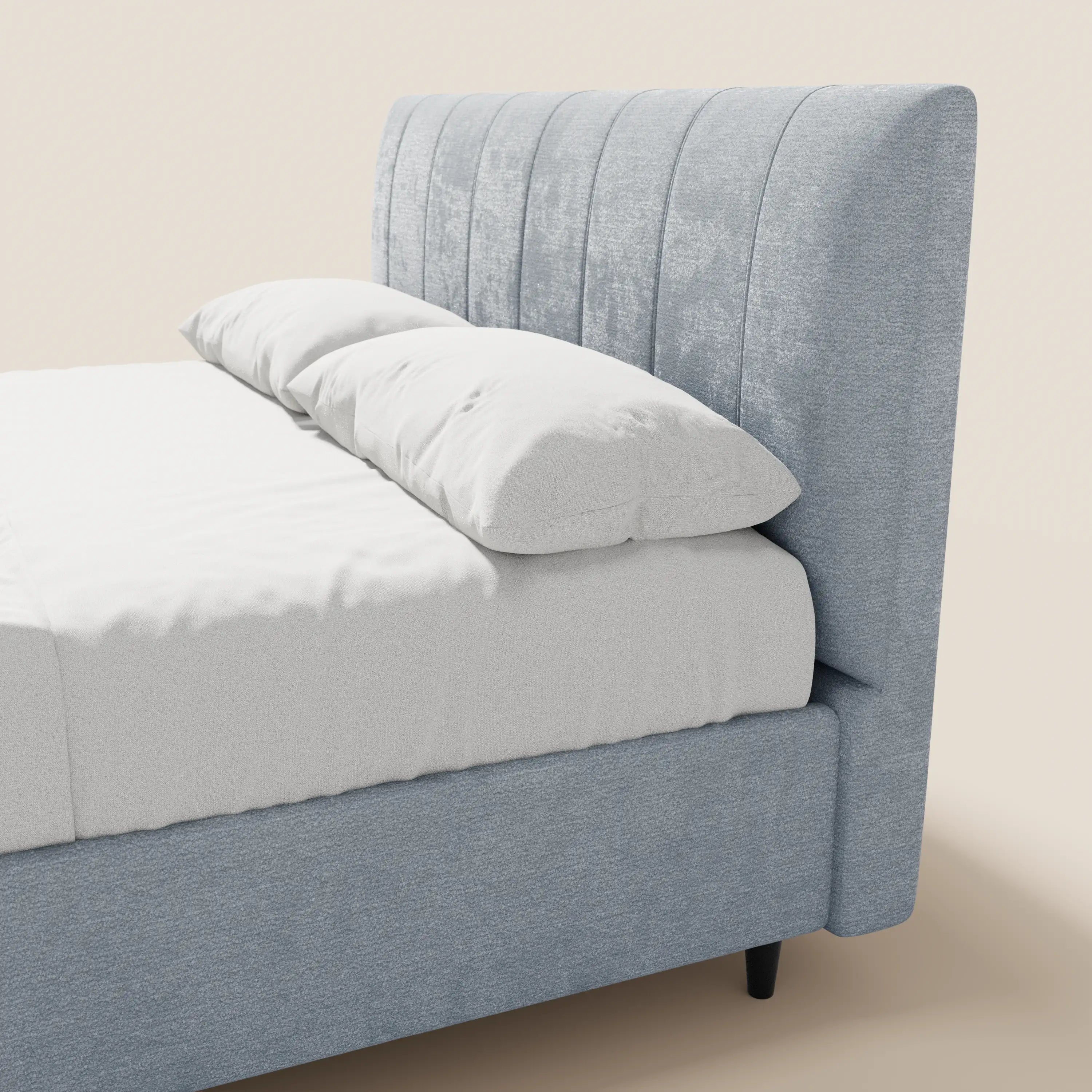 Il letto imbottito ONYX con contenitore di Letti.store presenta una struttura in tessuto azzurro certificato Oeko-Tex® e una testiera alta con canalature verticali. Nella foto è raffigurato con biancheria da letto e cuscini bianchi su uno sfondo beige a tinta unita.