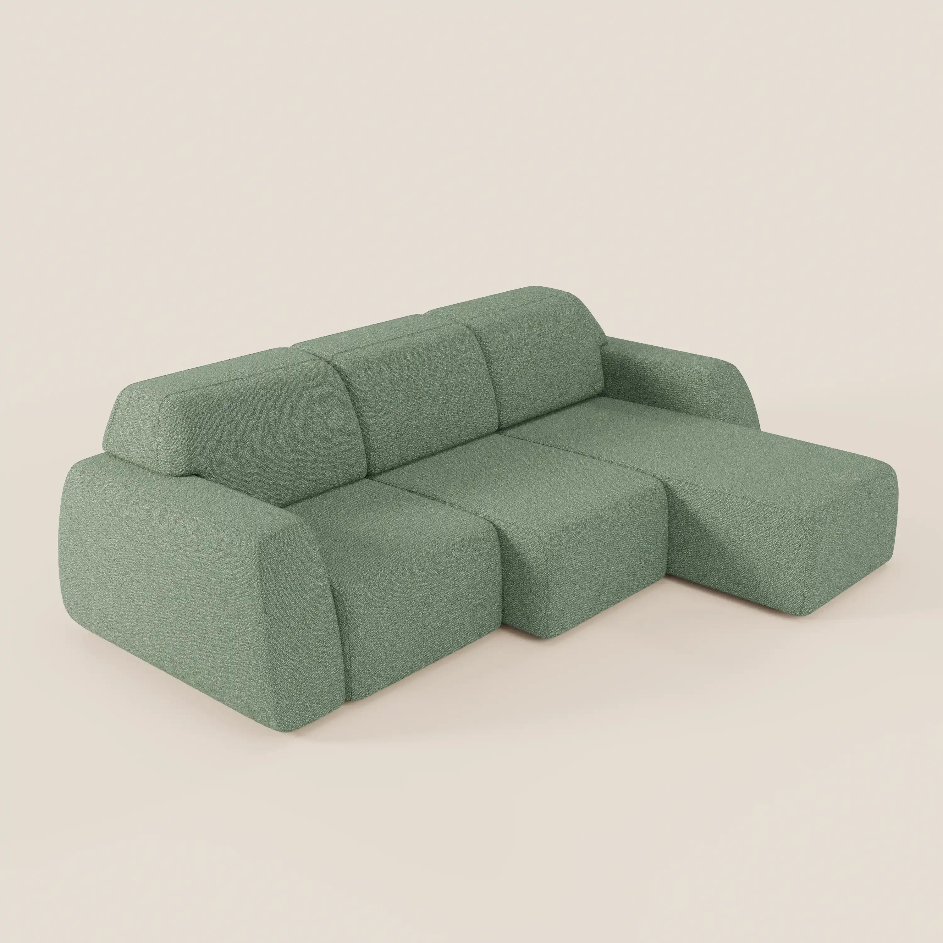 Il divano angolare Orbit di Divani.Store ha un design modulare verde salvia con una penisola reversibile, tre sedute allungabili in tessuto smacchiabile effetto cotone T33, bordi morbidi e arrotondati e stile minimal su sfondo beige chiaro.