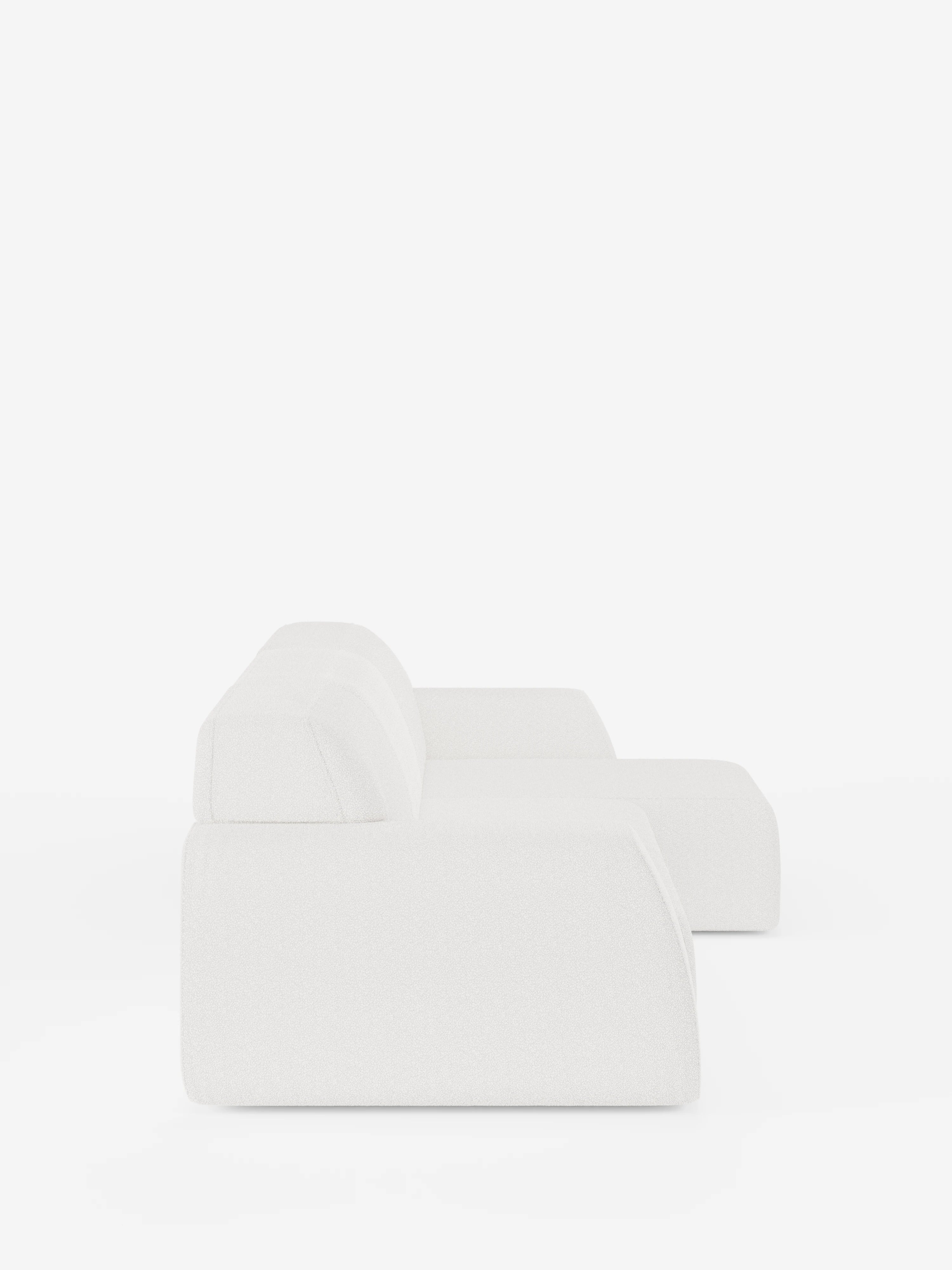 Un moderno e minimalista divano angolare Orbit bianco con penisola reversibile e tutte le sedute allungabili, rivestito in tessuto smacchiabile effetto cotone T33 di Divani.Store, è esposto su uno sfondo bianco a tinta unita. Questo divano componibile è caratterizzato da uno schienale basso, braccioli spessi e sedute allungabili, e viene ripreso in una ripresa laterale per evidenziarne la silhouette semplice ed elegante.
