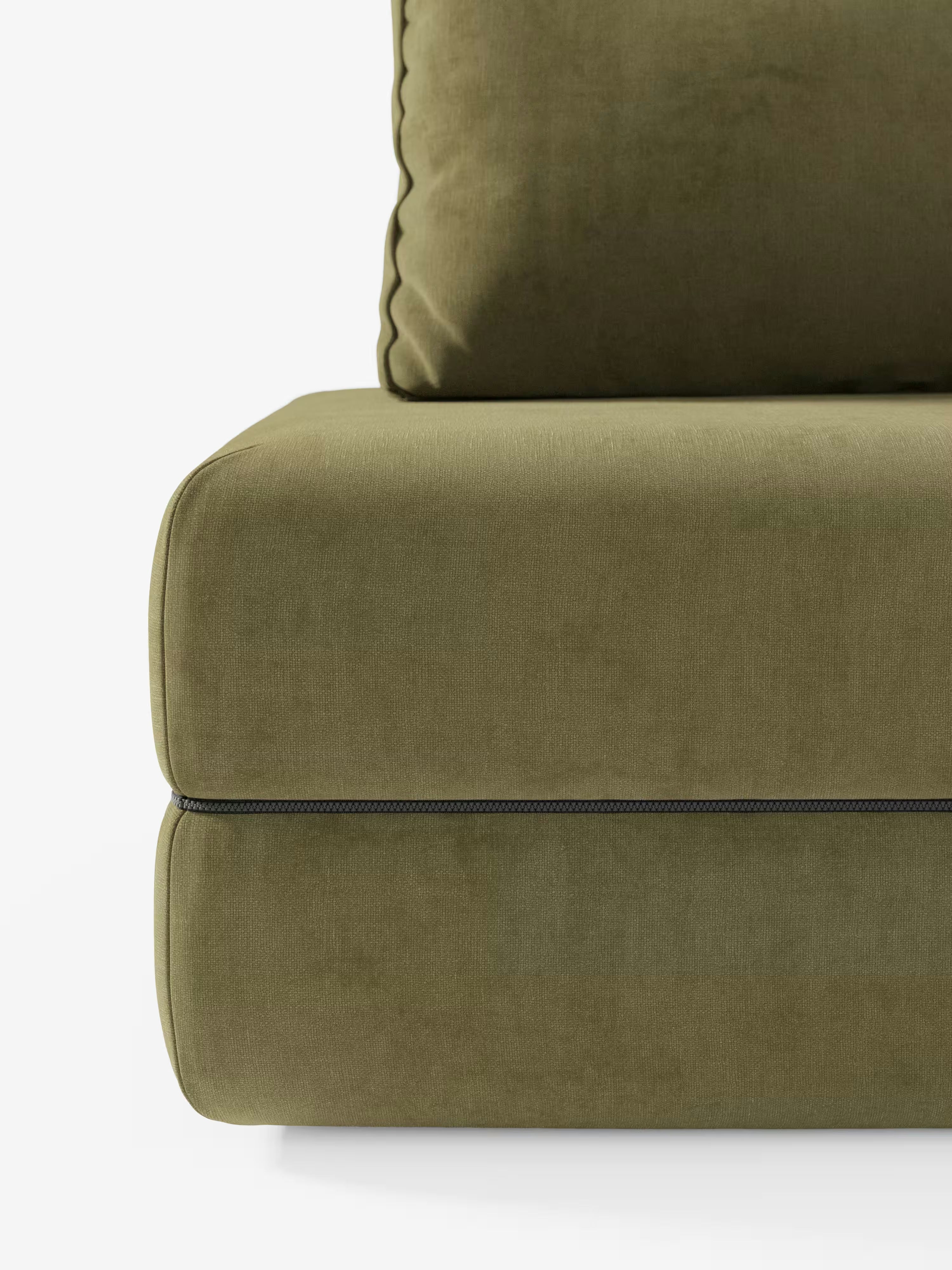Primo piano dei cuscini della seduta e dello schienale del divano letto matrimoniale Rift a 2 e 3 posti con schienali mobili di Divani.Store, in verde oliva; il tessuto T31, liscio e vellutato, è smacchiabile e presenta cuciture a vista e una cerniera nera che corre orizzontalmente tra i cuscini. Su uno sfondo bianco a tinta unita, questo raffinato dettaglio mette in risalto l’elegante design del divano, perfetto per qualsiasi ambiente contemporaneo.