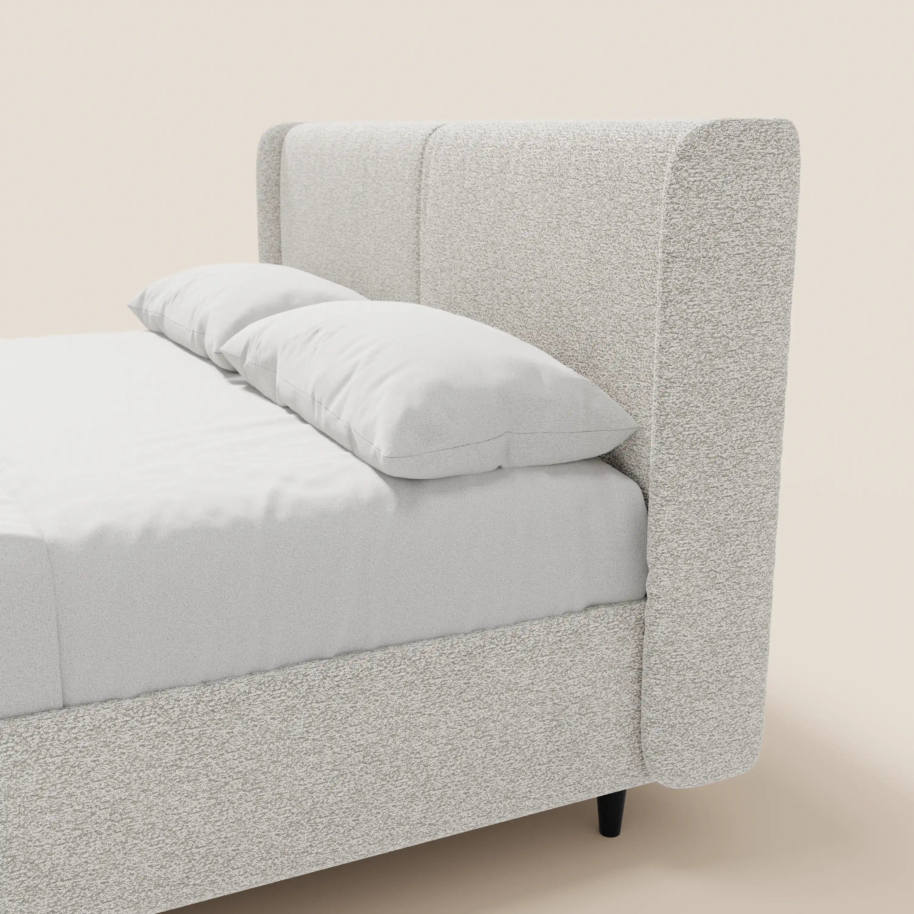 Il letto di design VALKIRIA di Letti.store è caratterizzato da una struttura leggera in tessuto Oeko-Tex®, una testiera avvolgente con 2 cuscini imbottiti e un vano contenitore. È presentato con biancheria da letto bianca a tinta unita, su gambe corte scure, su uno sfondo chiaro.