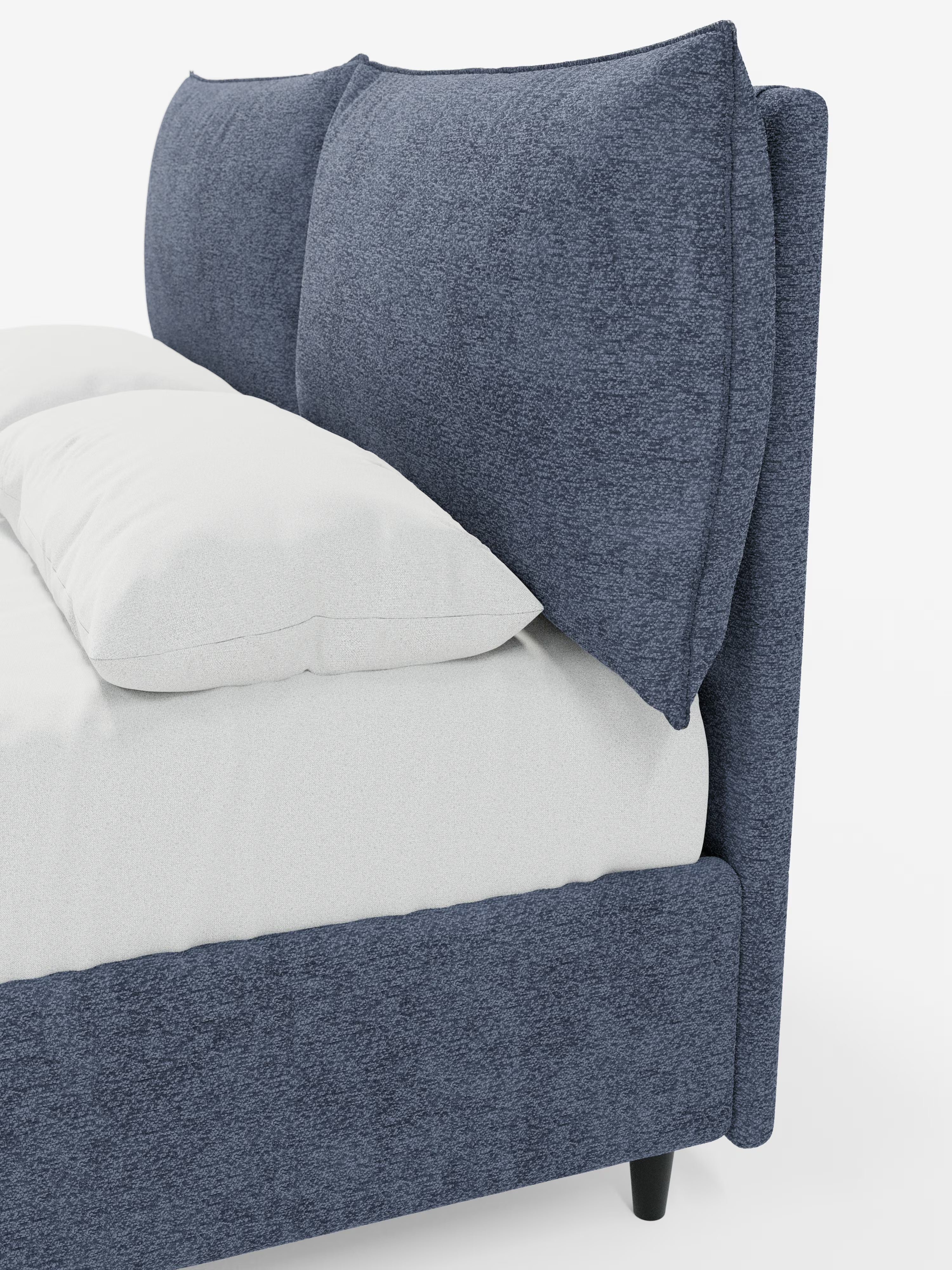 Primo piano del letto imbottito ZAYRON con vano contenitore e morbidi cuscini regolabili di Letti.store, caratterizzato da un design moderno in tessuto blu certificato Oeko-Tex®. La struttura e gli ampi e morbidi cuscini regolabili della testiera sono rivestiti in blu, mentre il materasso è coperto da un lenzuolo con angoli bianco. Il letto poggia su gambe nere ed è posizionato su uno sfondo bianco a tinta unita, con solo una parte del letto visibile.