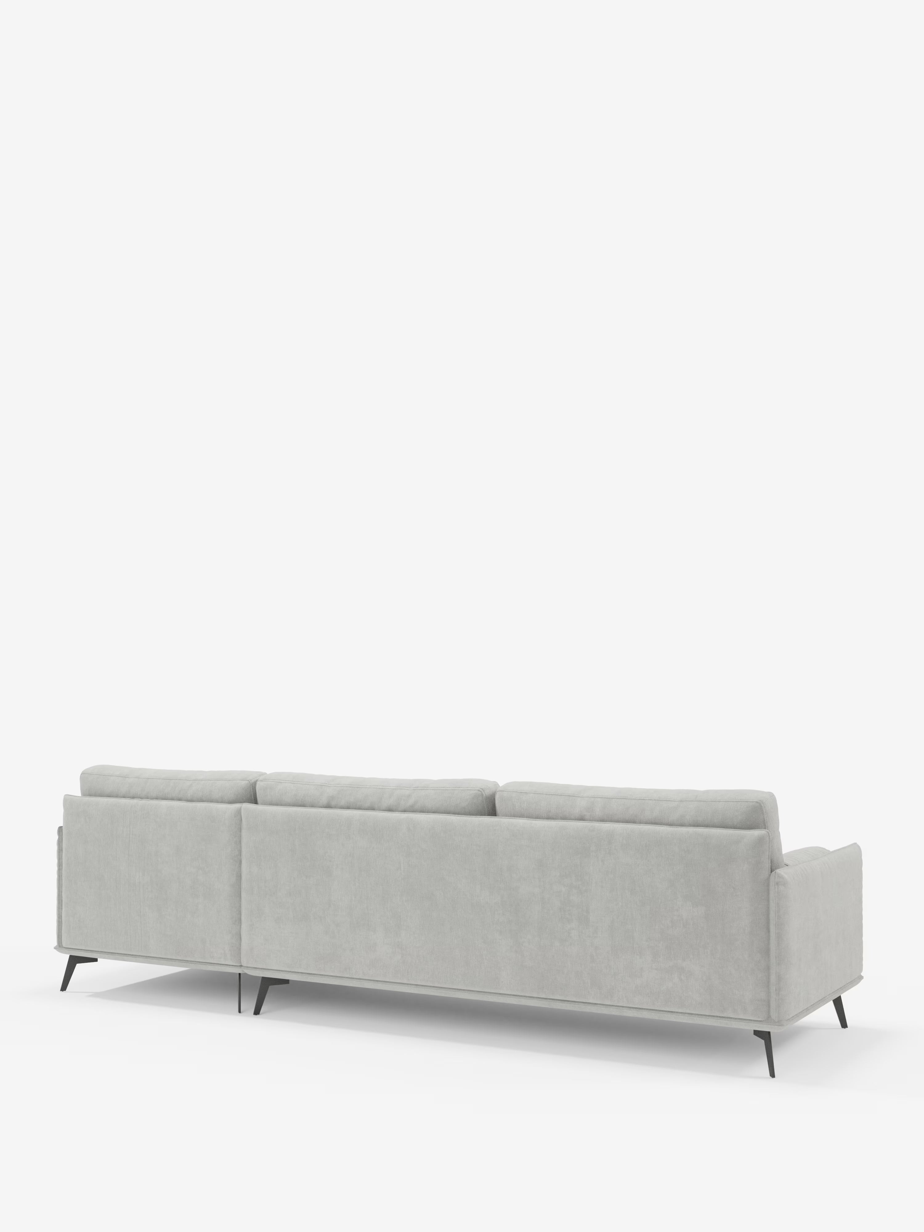 Un moderno divano a tre posti grigio chiaro, il “Basalto Divano moderno angolare con penisola” di Divani.Store, realizzato in Italia, è raffigurato di retro. Si caratterizza per un profilo basso, morbidi cuscini dello schienale imbottiti in piuma rivestiti in tessuto T31 di facile pulizia e un’elegante base in metallo con sottili gambe scure. Sullo sfondo bianco a tinta unita, le linee pulite e il design minimalista del divano risaltano con eleganza.