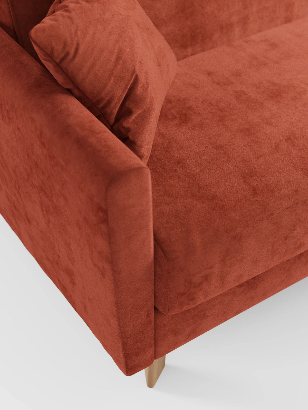 Primo piano di un divano letto Francy color ruggine con poggiatesta regolabili di Divani.Store, caratterizzato da un rivestimento sfoderabile al 100% in elegante tessuto T30 antimacchia e da un cuscino coordinato sulla seduta. Questo moderno divano a 2 o 3 posti vanta linee pulite e gambe in legno chiaro, che risaltano su uno sfondo bianco a tinta unita.