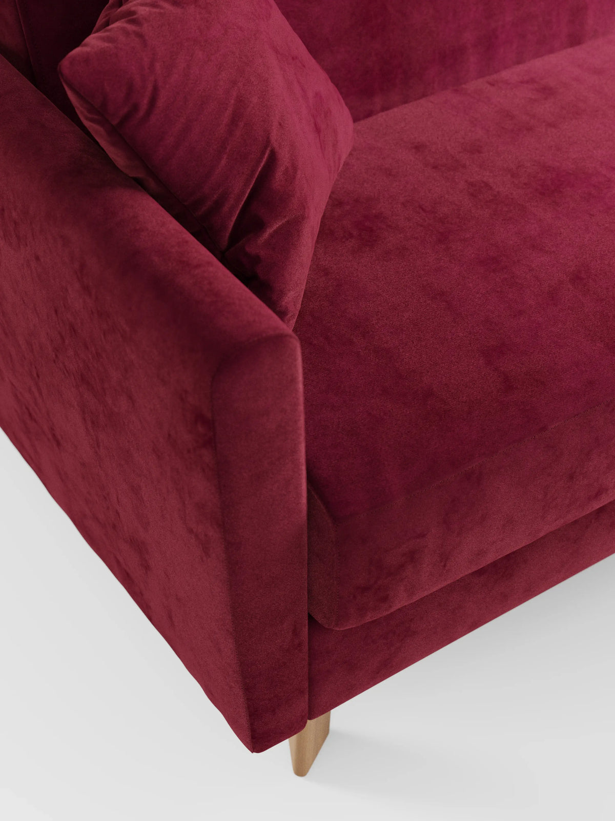 Un primo piano di una sezione angolare del divano letto Francy con poggiatesta regolabili di Divani.Store, rivestito in elegante tessuto T30 antimacchia di colore rosso intenso, con cuscino abbinato e gambe in legno chiaro, su uno sfondo bianco a tinta unita.