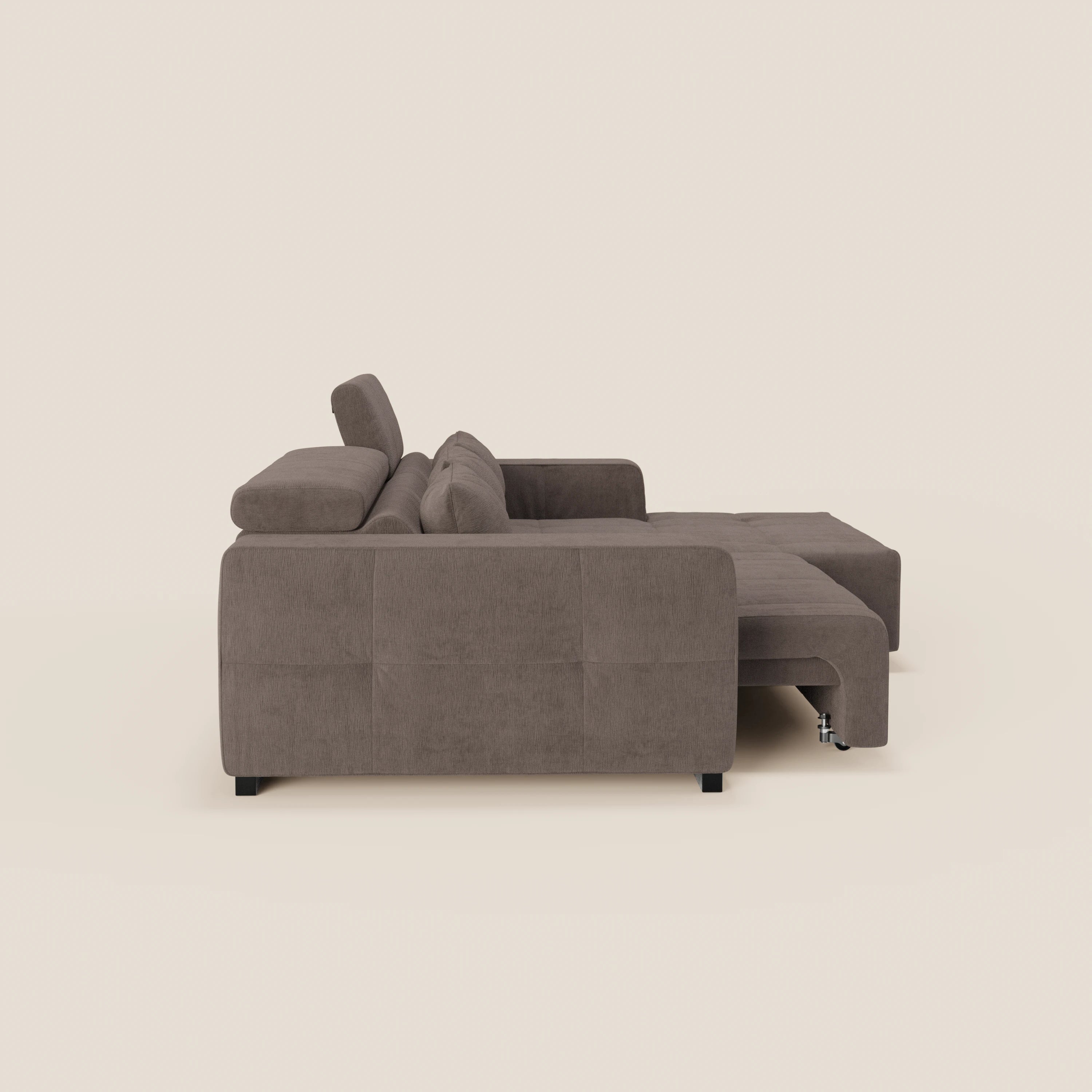 Vista laterale del Monarch Divano angolare con penisola e Relax Elettrico di Divani.Store, in morbido tessuto T31 antimacchia. Presenta cuscini rettangolari, braccioli, poggiatesta reclinabili, estensione della chaise e gambe corte nere su sfondo beige chiaro.