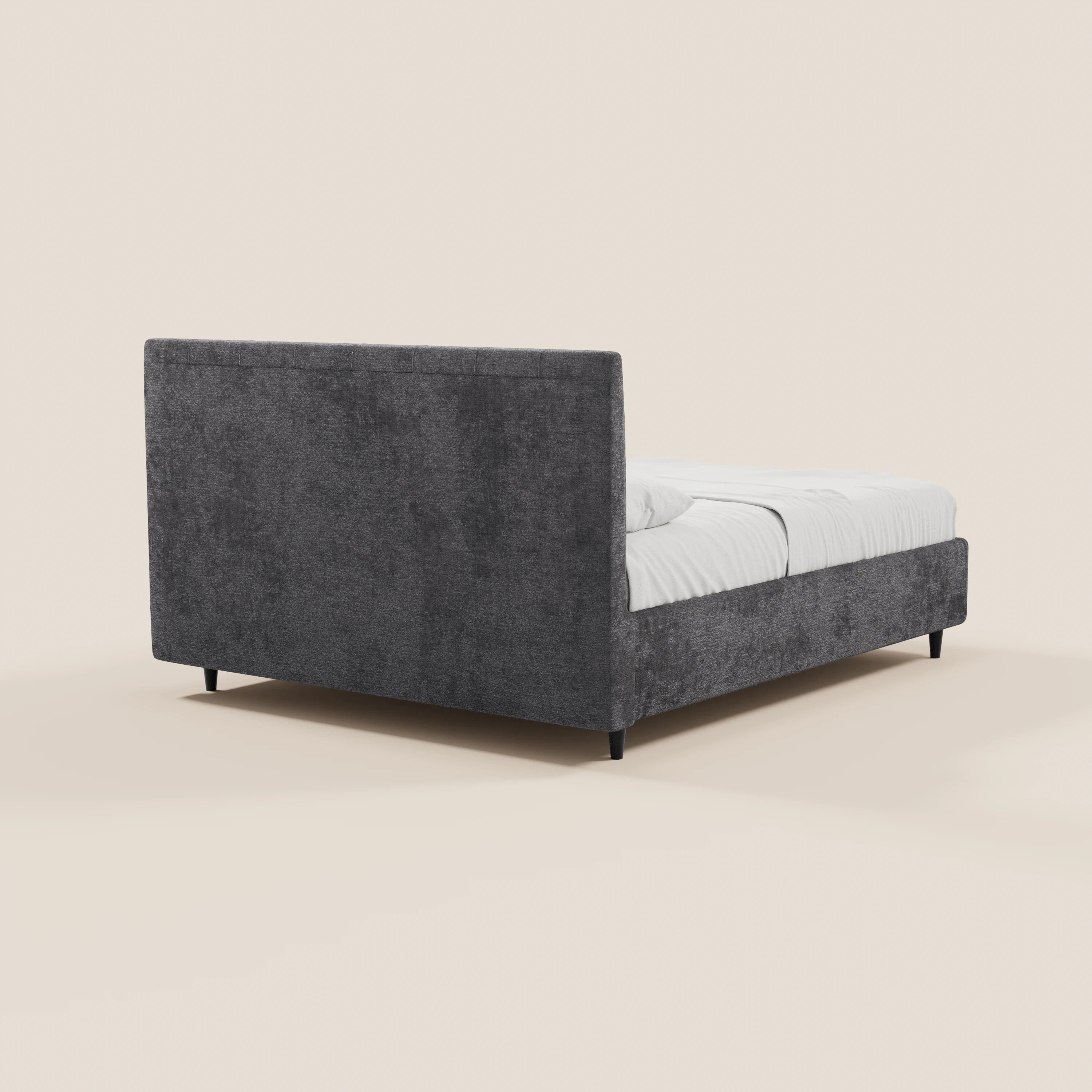 Il letto imbottito ONYX di Letti.store è realizzato in tessuto grigio scuro certificato Oeko-Tex®, con testiera alta verticale, pediera bassa e gambe corte nere. Immagine ripresa dal lato posteriore destro con biancheria da letto bianca, su uno sfondo beige a tinta unita.