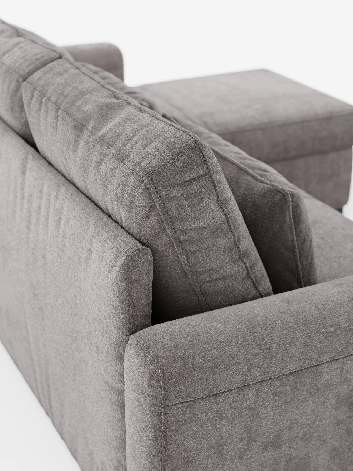 Una vista dall'alto del divano letto Ottaviano con letto estraibile - penisola reversibile e contenitore in tessuto materico smacchiabile, un divano componibile grigio con tessuto materico, due cuscini dello schienale spessi e una chaise longue sul lato destro di colore bianco.