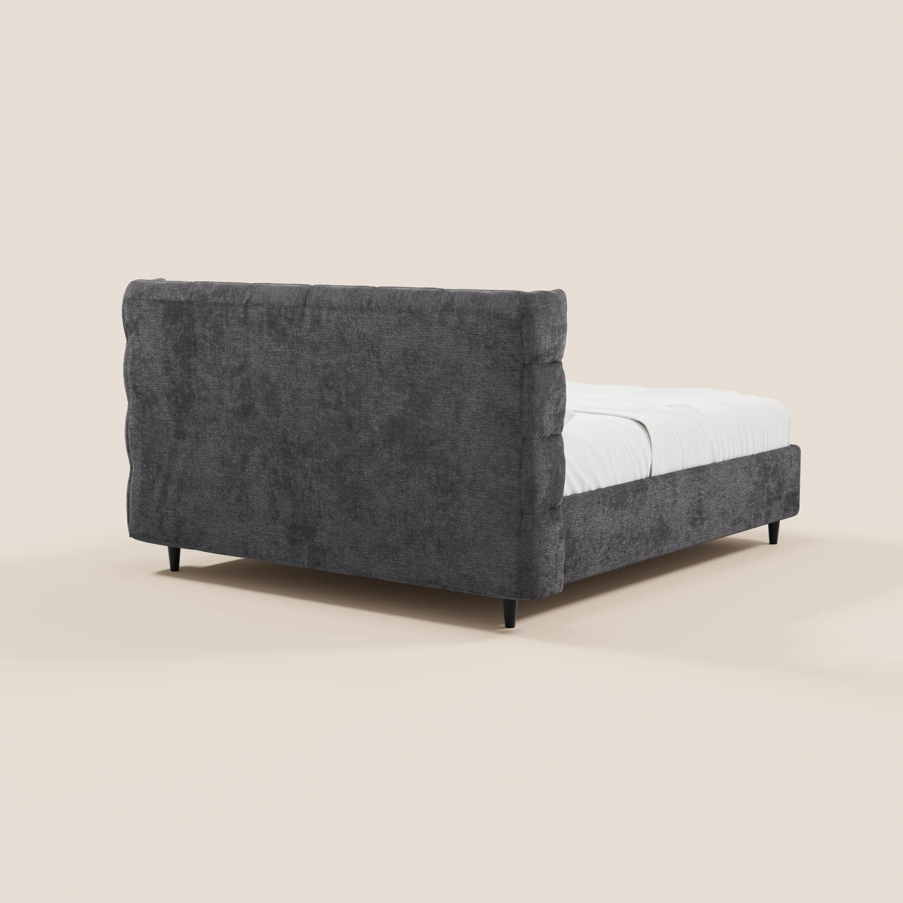 Il letto imbottito RAGNAR di Letti.store è caratterizzato da un tessuto grigio scuro certificato Oeko-Tex®, una testiera avvolgente capitonné e pannelli laterali trapuntati, il tutto sostenuto da quattro gambe nere. La biancheria da letto bianca ne esalta lo stile moderno e accogliente sullo sfondo di un beige chiaro.