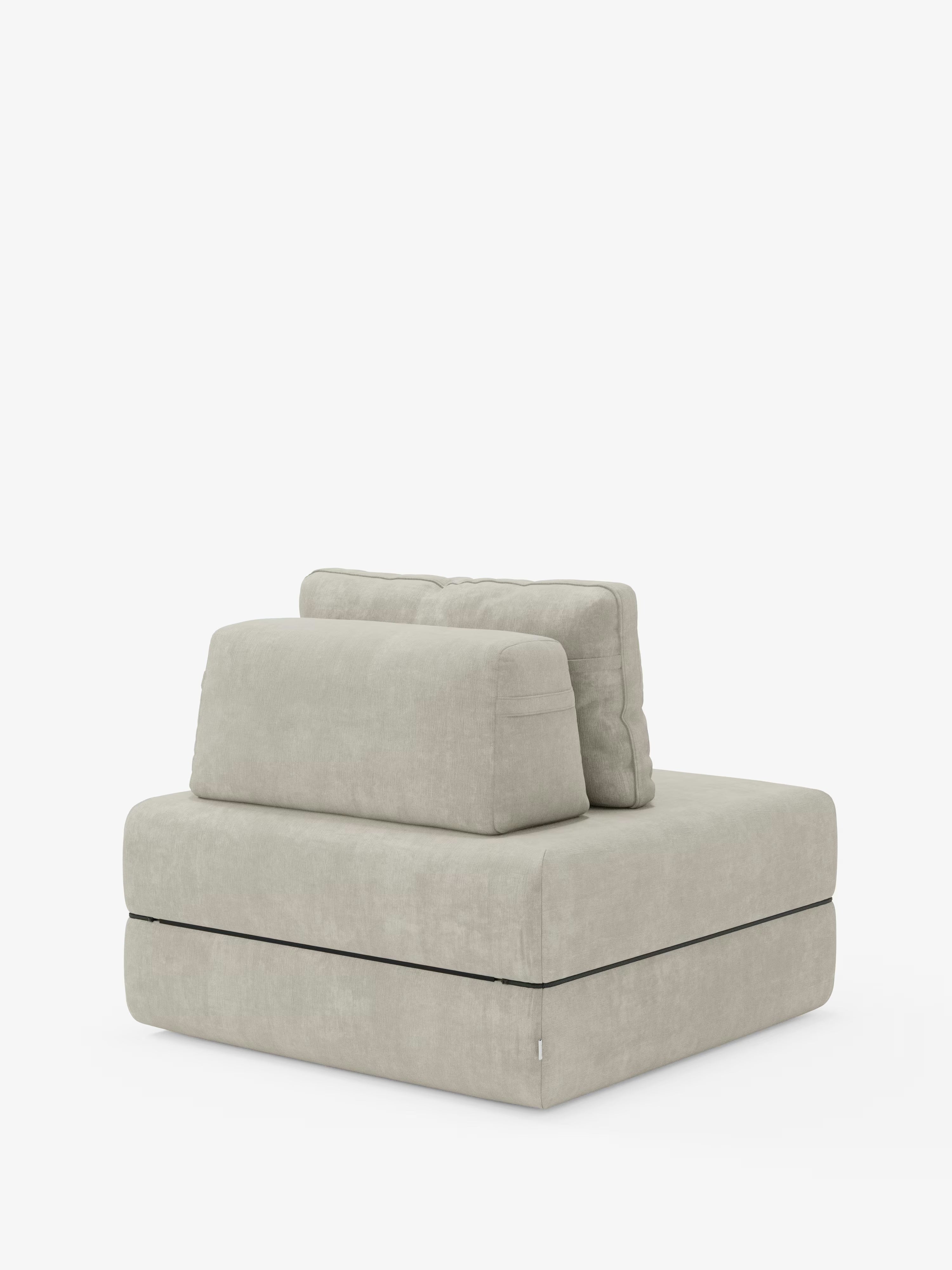 Una poltrona senza braccioli contemporanea, rivestita in grigio chiaro, di Divani.Store: la Rift, poltrona letto con materasso alto 24 cm e memory foam, presenta una silhouette squadrata e minimalista ispirata al design delle poltrone letto. Con un cuscino dello schienale rettangolare rimovibile, un cuscino di seduta spesso e un cuscino inferiore staccabile — tutti realizzati con linee pulite in tessuto T31 facile da pulire — si staglia con eleganza su uno sfondo bianco.