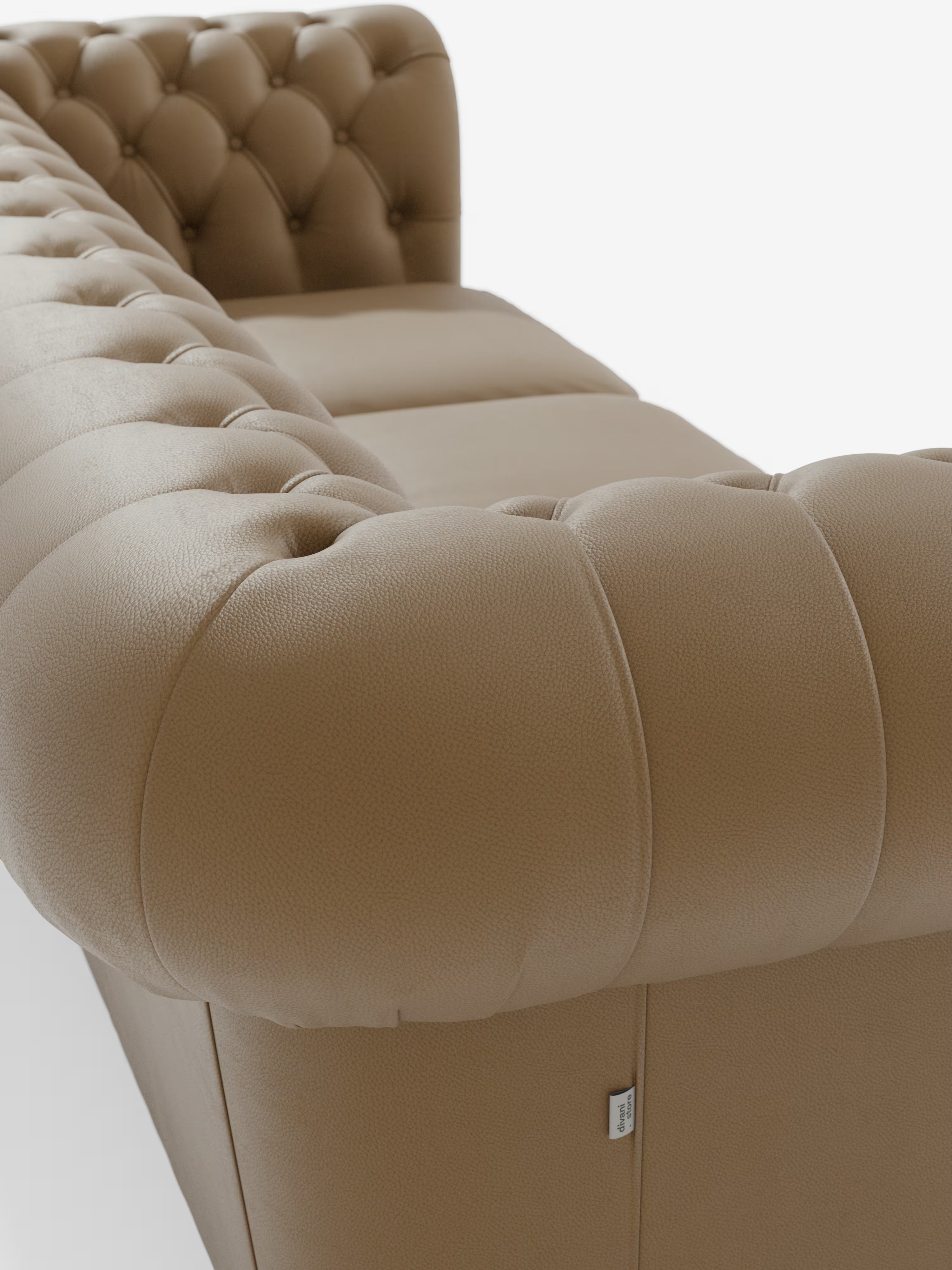 Chester 4 posti, 3 sedute in vera pelle – Chesterfield capitonné artigianale di Divani.Store, raffigurato in pelle color cuoio in un primo piano dal lato posteriore, mette in risalto la profonda trapuntatura dello schienale e dei braccioli, i morbidi cuscini di seduta in vera pelle e una piccola etichetta in tessuto bianco sul lato. Questo elegante divano è stato fotografato su uno sfondo bianco e pulito in studio.