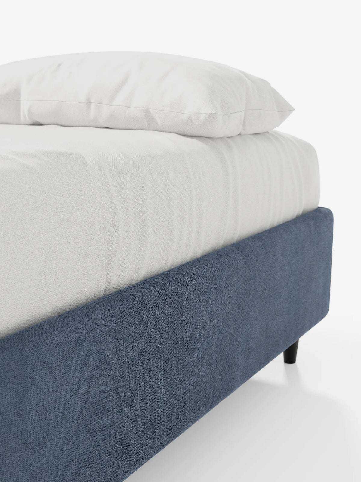 Un primo piano dell'angolo imbottito blu con trama in rilievo di un letto sommier ERON con contenitore, rivestito in tessuto impermeabile certificato Oeko-Tex, poggiato su gambe scure con un materasso coperto da un lenzuolo bianco su uno sfondo bianco.