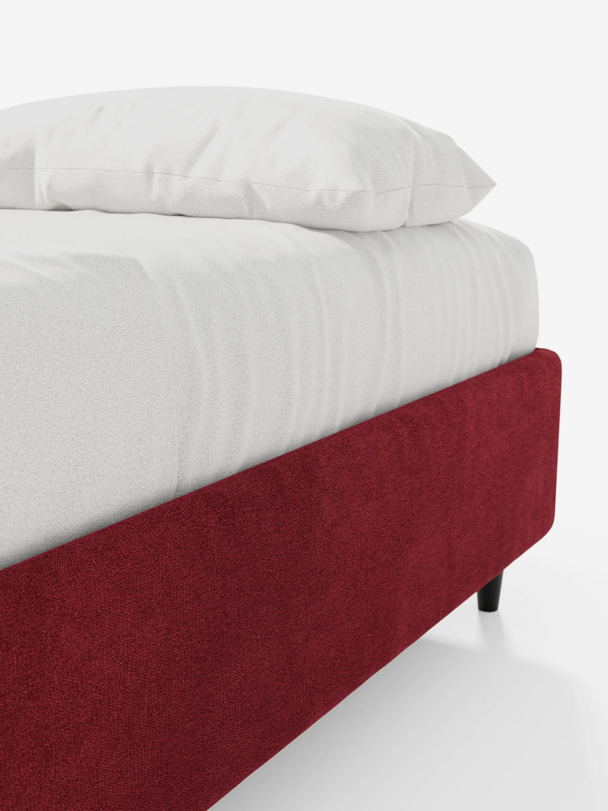 Un primo piano di una struttura letto ERON rosso, modello “letto sommier” imbottita con vano contenitore in tessuto impermeabile certificato Oeko-Tex, su gambe nere, con sopra un materasso bianco e un cuscino, su uno sfondo chiaro.