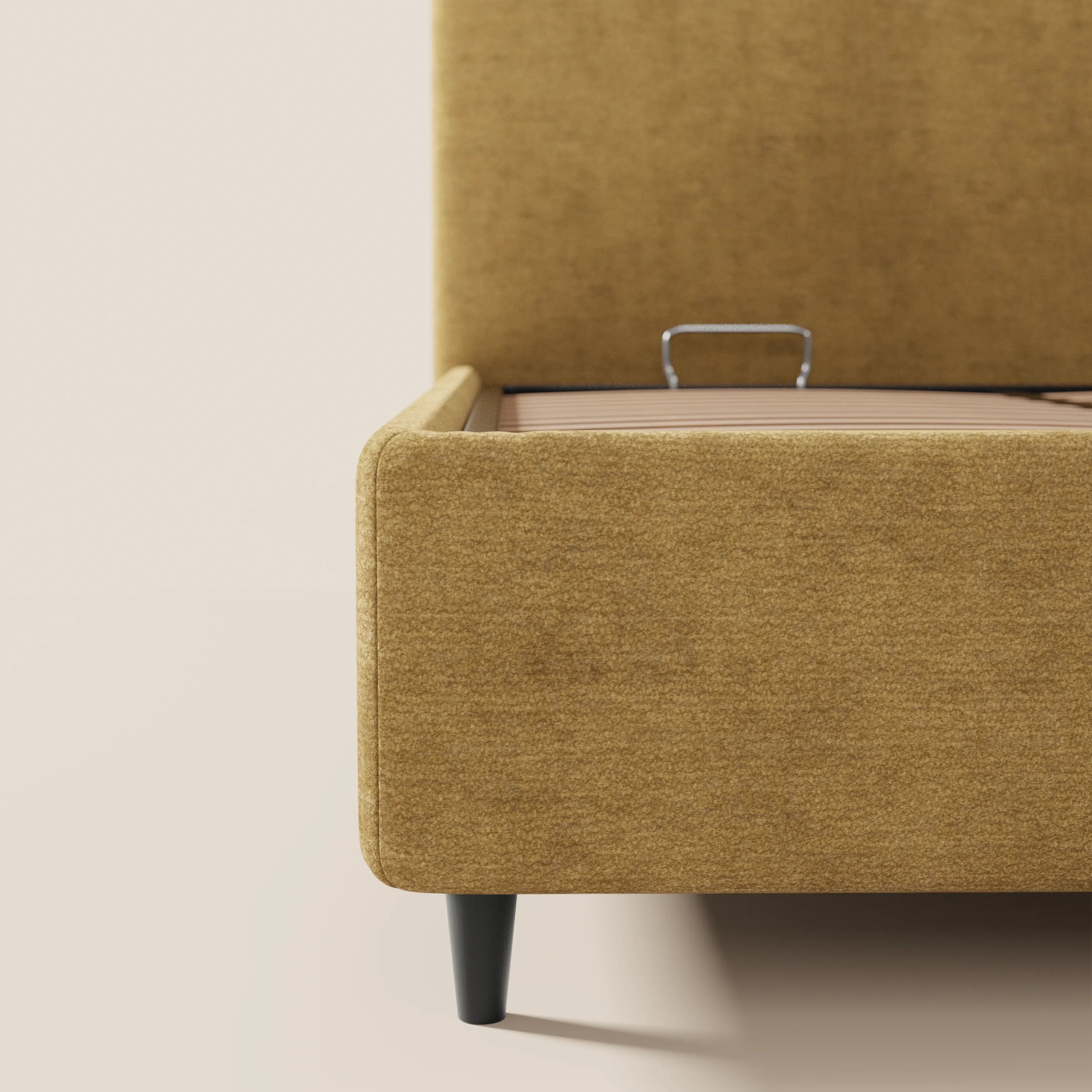 Primo piano del letto imbottito KAELOS Letto Minimal di Letti.store, in ciniglia color senape, con gambe alte nere, testiera arrotondata e vano contenitore aperto sotto il letto con maniglia in metallo. Immagine su sfondo bianco sporco.