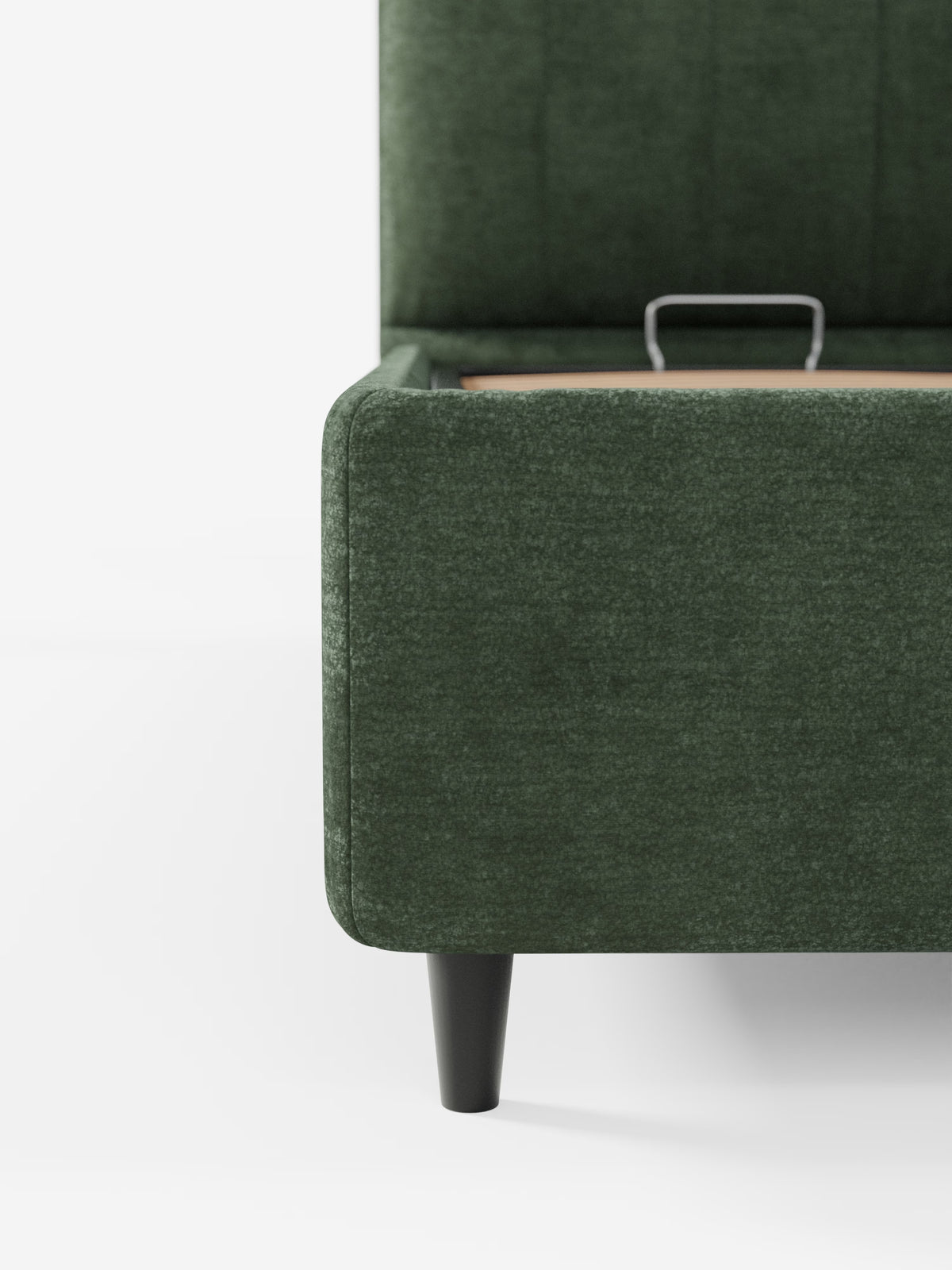Primo piano del letto imbottito ONYX con vano contenitore e testiera verticale in tessuto certificato Oeko-Tex® di Letti.store, rivestito in tessuto verde scuro. L'immagine mette in risalto l'angolo con il coperchio del vano contenitore parzialmente aperto, evidenziando le sue gambe affusolate nere su uno sfondo bianco a tinta unita.