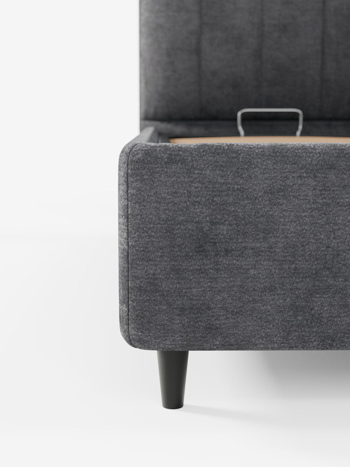 Primo piano del letto imbottito ONYX con contenitore e testiera verticale in tessuto certificato Oeko-Tex® di Letti.store, caratterizzato da un angolo rivestito in tessuto grigio scuro con una gamba nera a vista e una maniglia interna in metallo, su uno sfondo bianco a tinta unita.