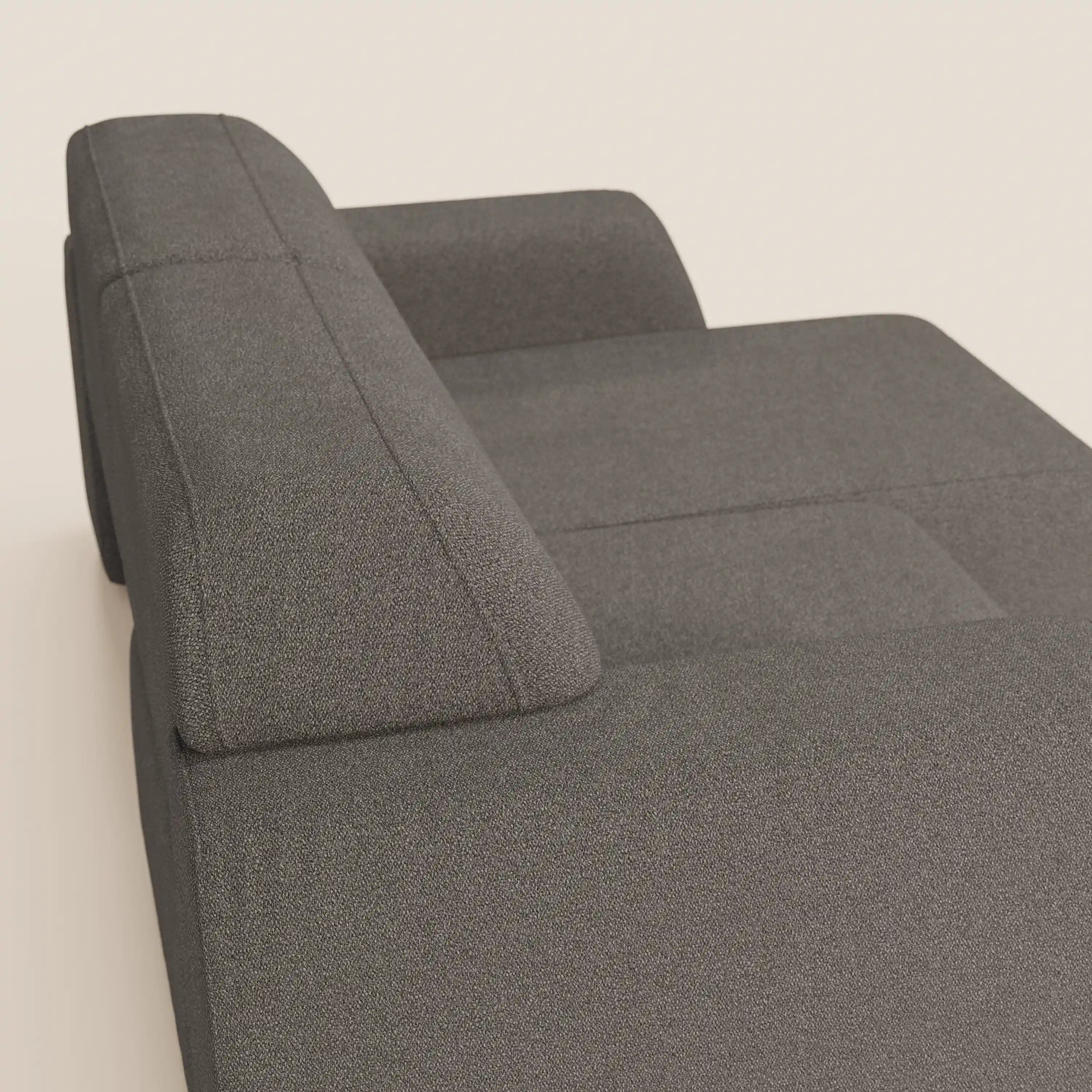 Un primo piano del divano Orbit 2 e 3 posti di Divani.Store mostra il tessuto grigio effetto cotone T33 e gli ampi braccioli. Il suo look minimalista risalta su una parete beige semplice. Rivestimento completamente sfoderabile e antimacchia.