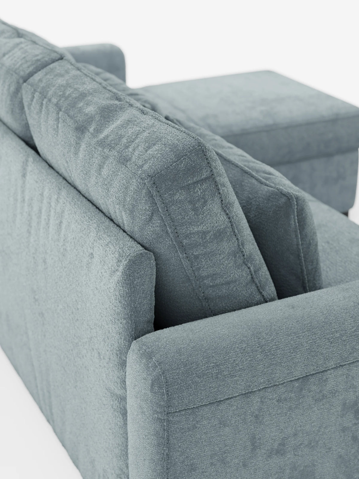 Un primo piano di un divano letto Ottaviano azzurro con letto estraibile – penisola reversibile e contenitore in tessuto materico smacchiabile, che mette in risalto i cuscini dello schienale dalla trama particolare, gli ampi braccioli e la chaise longue su uno sfondo bianco.