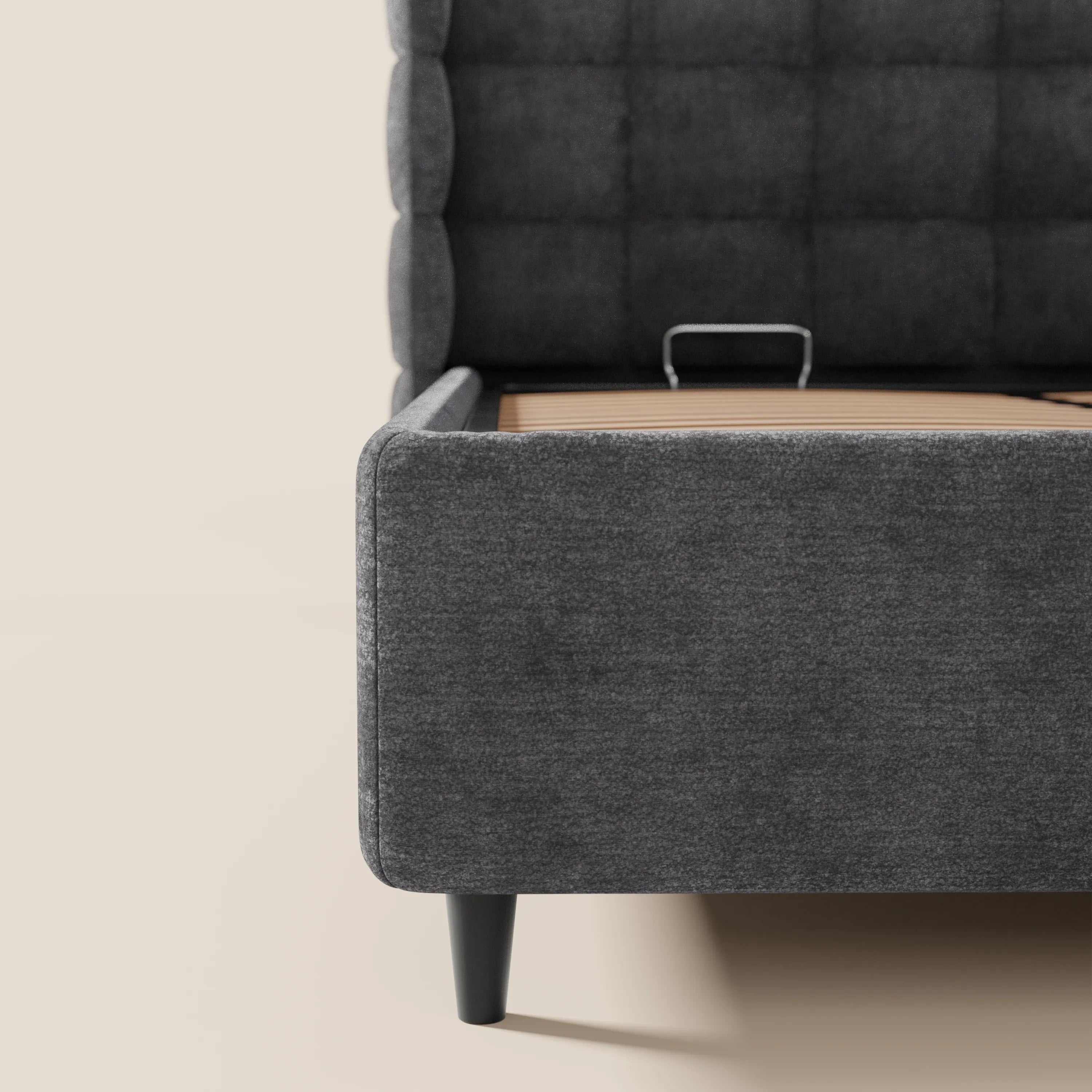 Primo piano del letto imbottito RAGNAR con contenitore di Letti.store, realizzato in elegante tessuto Oeko-Tex®, con testiera capitonné avvolgente, gambe nere corte e senza materasso, che mostra la struttura interna in legno e metallo.