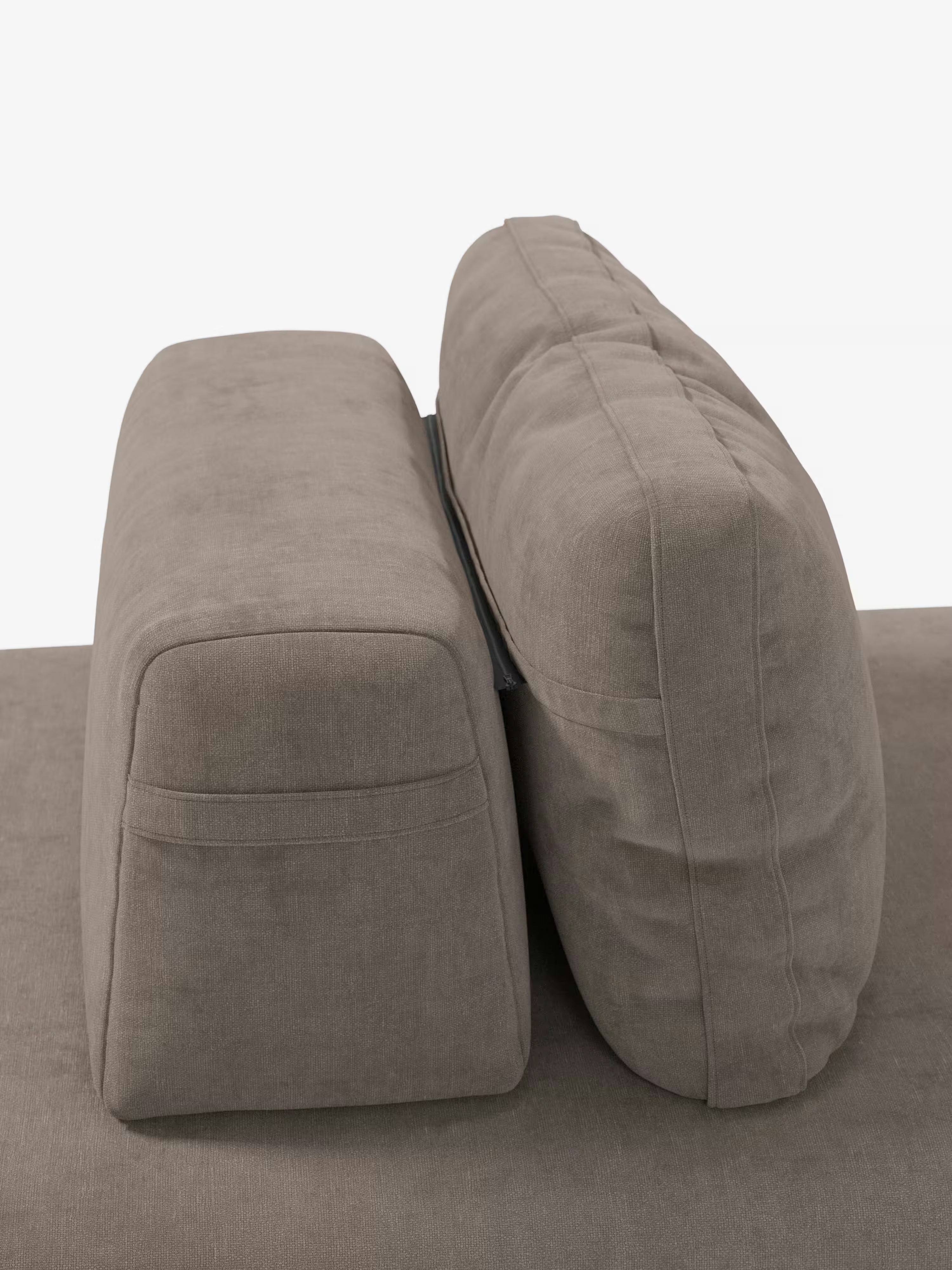 Due cuscini rettangolari color taupe della linea “Rift” di Divani.Store, relativa al divano letto matrimoniale a 2 e 3 posti con schienali mobili, sono disposti in posizione verticale uno accanto all’altro. Il cuscino a sinistra è più corto e squadrato, mentre quello a destra è più alto e arrotondato. Entrambi presentano cuciture a vista e mettono in risalto gli schienali mobili caratteristici di questo design contemporaneo. Lo sfondo è bianco a tinta unita.