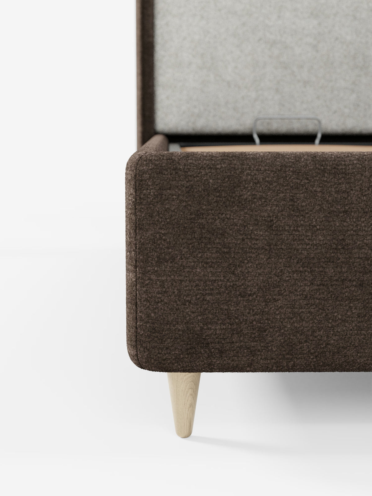 Primo piano di una panca contenitore imbottita marrone con gambe in legno chiaro. Il coperchio è aperto e rivela un interno rivestito in tessuto grigio chiaro e una piccola maniglia in metallo all’interno: un’elegante soluzione contenitiva ispirata al design pratico del letto imbottito bicolore con vano contenitore VALKIRIA di Letti.store, con la sua caratteristica testiera curva e i cuscini dello schienale inclusi. Lo sfondo è bianco a tinta unita.