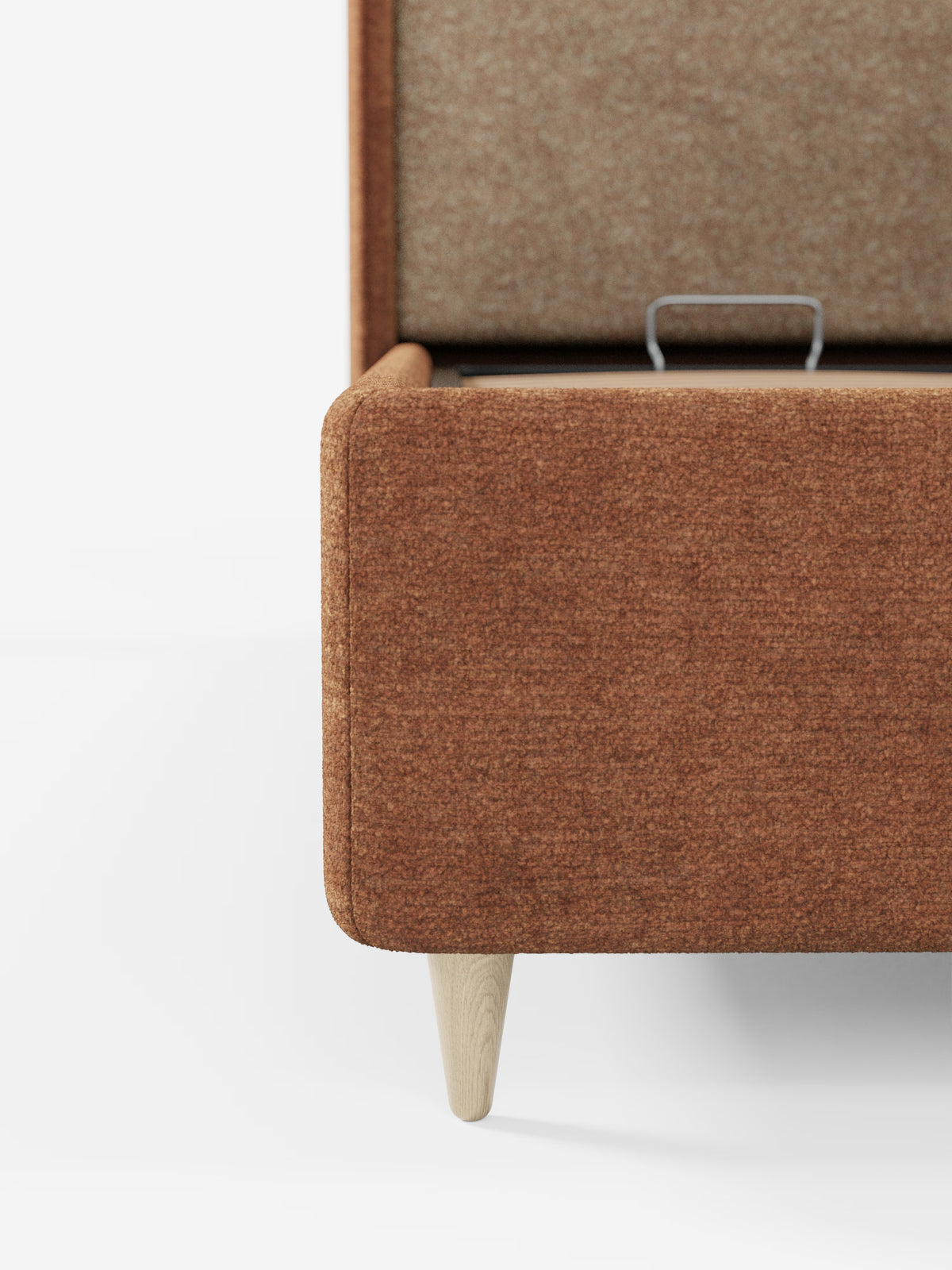 Un primo piano del letto imbottito bicolore con vano contenitore VALKIRIA di Letti.store, che mette in risalto il rivestimento color ruggine e le gambe in legno chiaro. Il coperchio è aperto e rivela un vano contenitore rivestito in tessuto con una maniglia in metallo. Su uno sfondo bianco, l’immagine mette in risalto le linee morbide della panca, che richiamano la testiera curva avvolgente e i cuscini dello schienale, evocando un elegante letto imbottito italiano con contenitore.