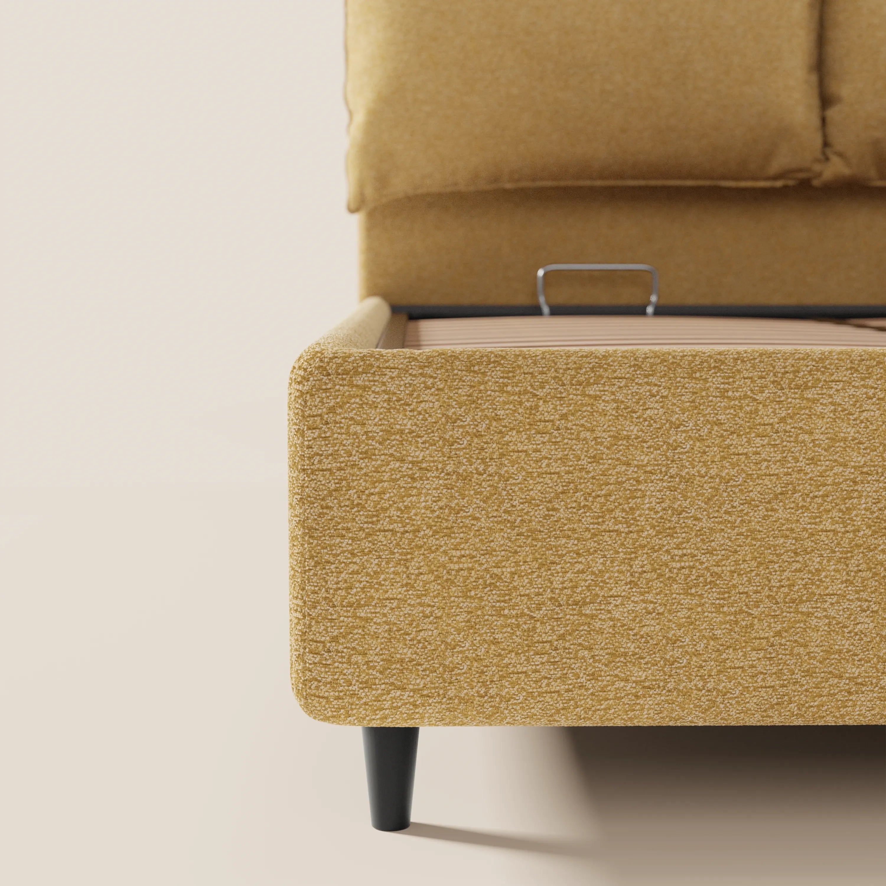 Primo piano del letto imbottito ZAYRON di Letti.store in tessuto giallo senape certificato Oeko-Tex®, che mostra le sue gambe corte nere, una testata parzialmente regolabile con cuscino e una maniglia interna che facilita l'accesso al vano contenitore.