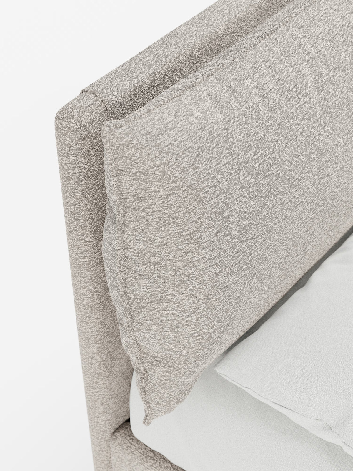 Primo piano del letto imbottito ZAYRON con contenitore e morbidi cuscini regolabili di Letti.store, che presenta una testiera contemporanea in tessuto certificato Oeko-Tex® in una tonalità di beige chiaro, morbida e dalla trama particolare, con un cuscino spesso appoggiato contro di essa. La biancheria da letto è di colore grigio chiaro, il tutto su uno sfondo bianco a tinta unita.
